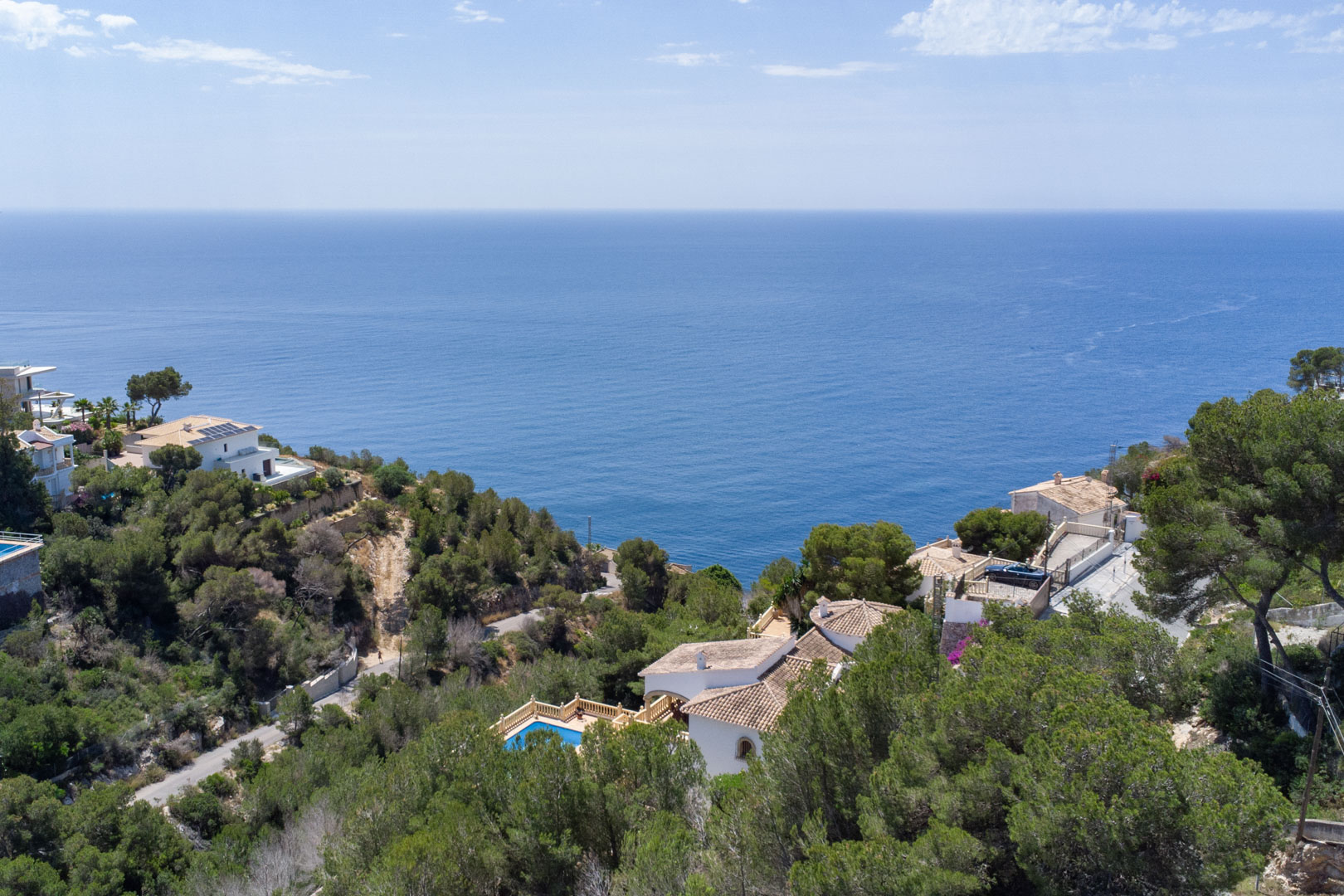 Vista aérea panorámica del mar Mediterráneo desde la urbanización Costa Nova, mostrando la densa vegetación de pinos y villas cercanas a la costa de Jávea.