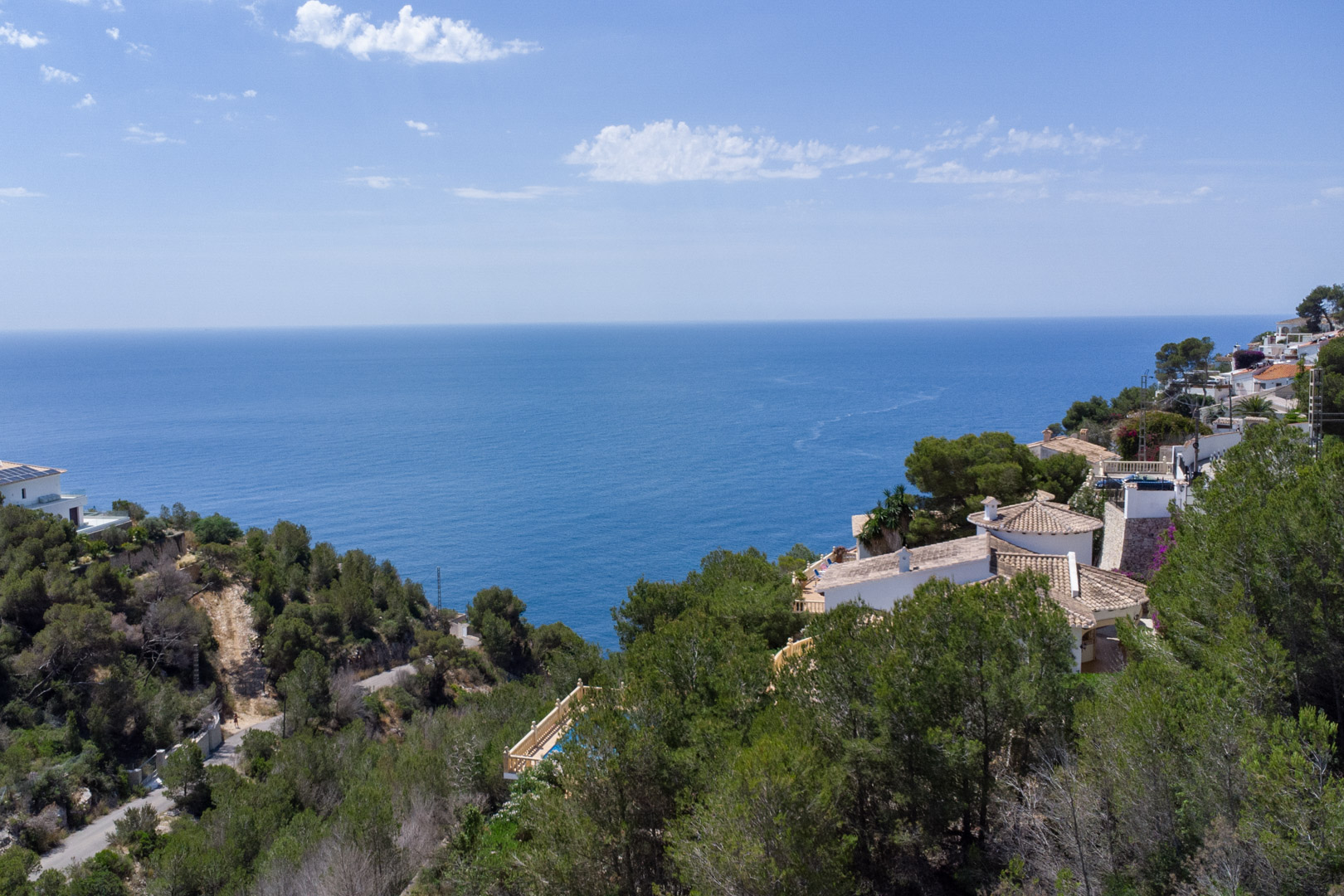 Vista panorámica del mar Mediterráneo desde la zona elevada de Costa Nova, mostrando la costa arbolada y las viviendas residenciales circundantes en Jávea.