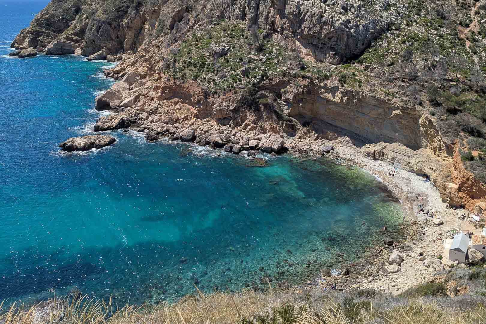 Vista de la Cala Llebeig con aguas cristalinas y acantilados de piedra caliza, accesible por un sendero cercano a la parte posterior de la vivienda.