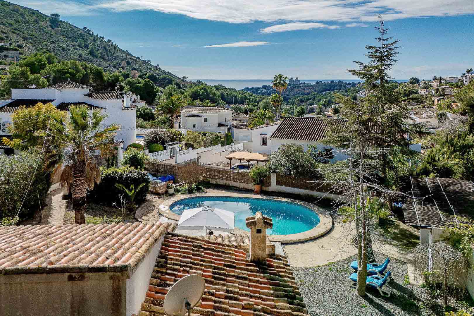 Vista elevada que muestra la piscina privada en forma de riñón rodeada de vegetación mediterránea, con vistas panorámicas al mar y al entorno residencial de Moraira.