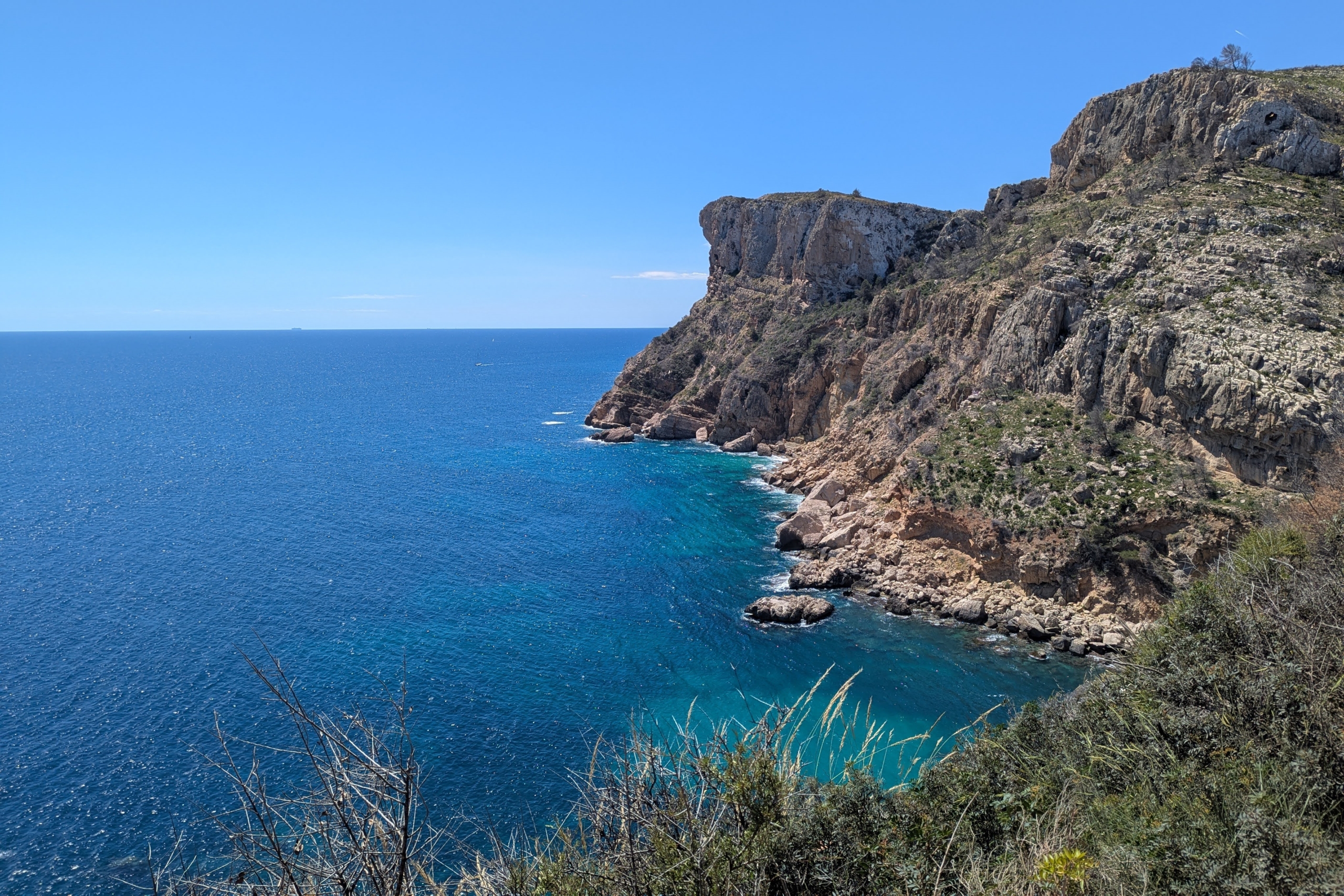Vistas panorámicas de los acantilados de piedra caliza y las aguas turquesas del Mediterráneo cerca de Cala Llebeig, rodeadas de vegetación autóctona.
