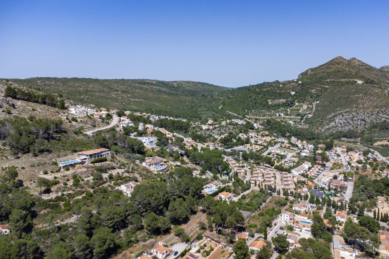 Vista aérea panorámica de Alcalalí que muestra la integración de las viviendas en la ladera, rodeadas de vegetación mediterránea y extensas vistas al valle.