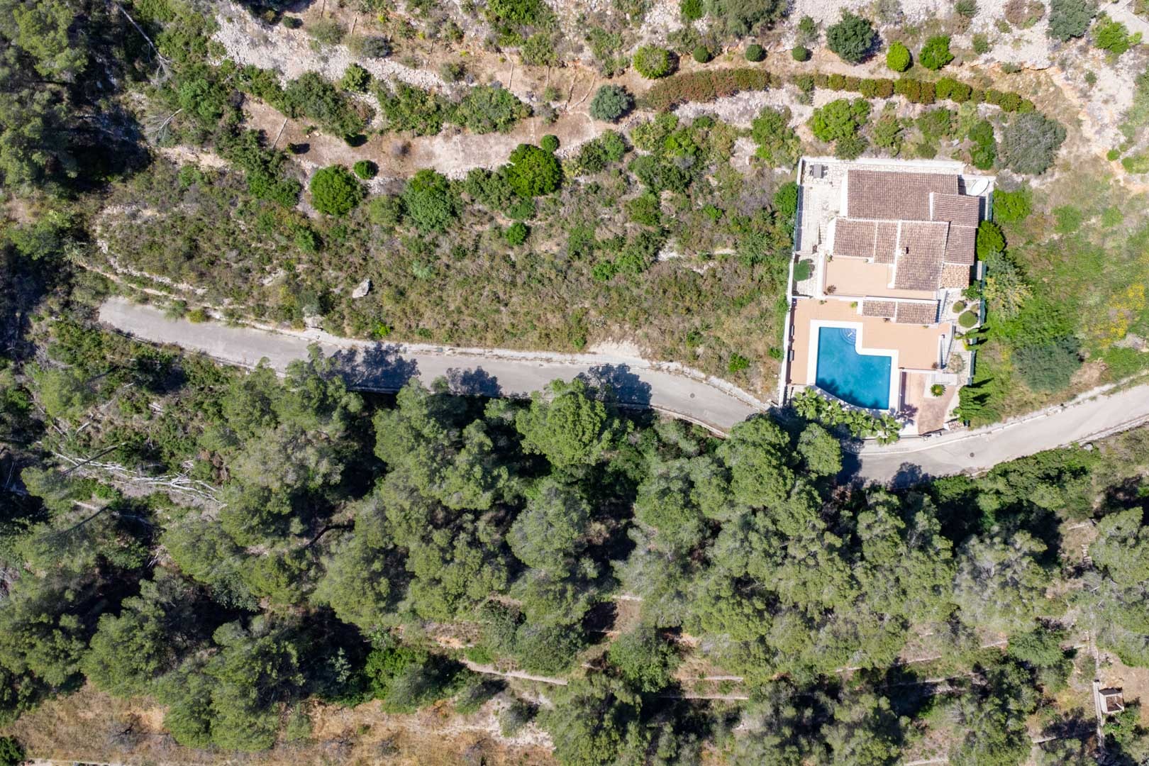Vista aérea de una villa independiente con piscina privada, integrada en un entorno natural boscoso con acceso privado pavimentado.