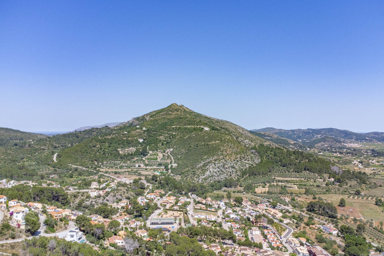 Vista aérea panorámica del pueblo de Alcalalí y el valle de Jalón, destacando el relieve montañoso mediterráneo y la integración de las viviendas en el entorno natural.