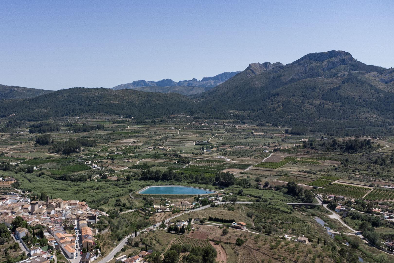 Vista aérea panorámica del valle de Jalón desde Alcalalí, mostrando el entorno natural, campos agrícolas y las montañas circundantes bajo un cielo despejado.
