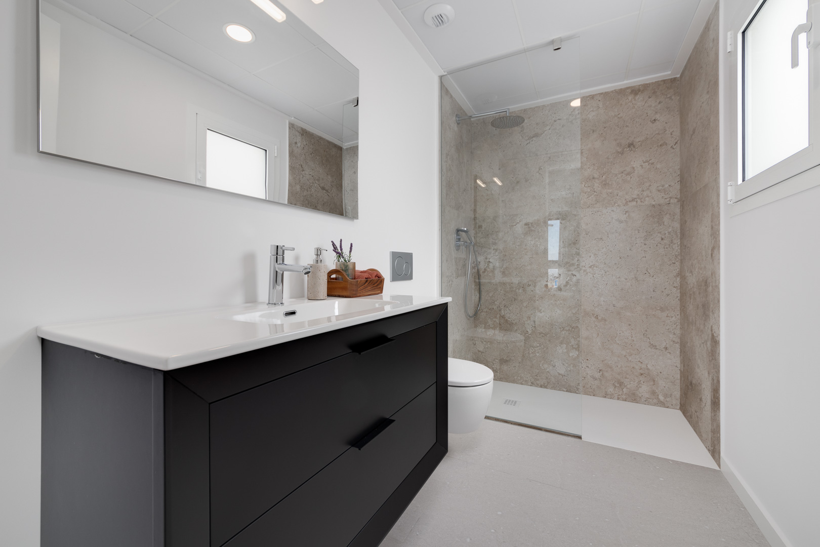 Baño contemporáneo con mueble de lavabo negro, ducha de obra con revestimiento porcelánico efecto piedra y mampara de cristal fija.