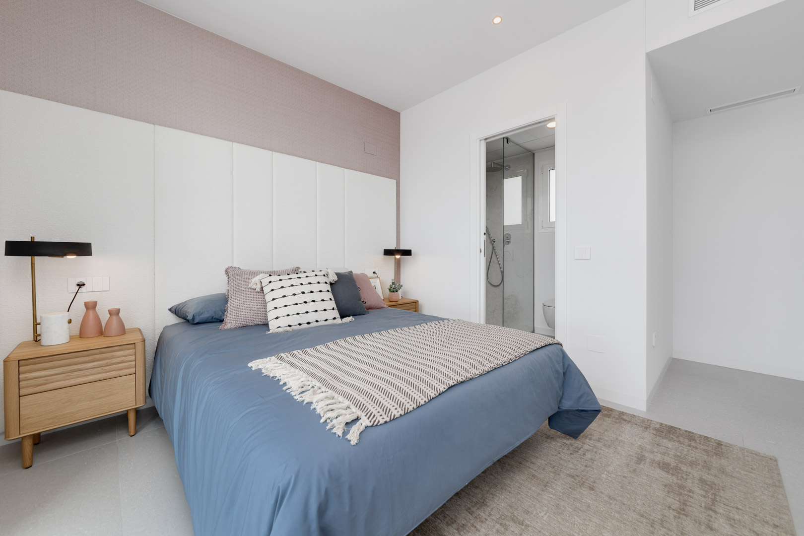 Dormitorio contemporáneo con cabecero panelado blanco, pared de acento en tono malva y baño en suite integrado con mampara de cristal.