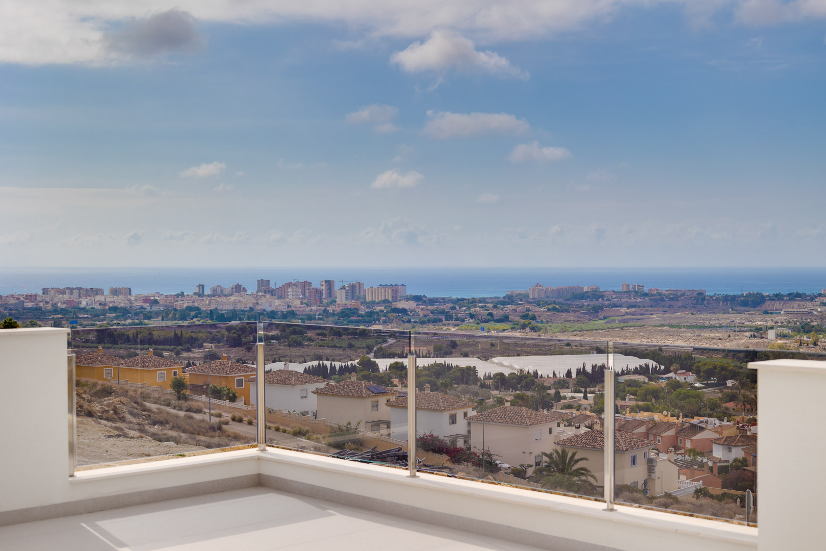 Terraza superior con suelo cerámico claro y barandilla de cristal, ofreciendo vistas panorámicas ininterrumpidas hacia la costa y el mar Mediterráneo.