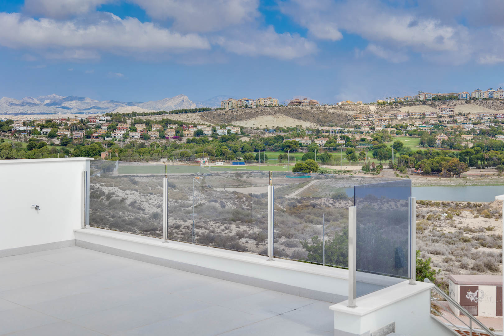 Terraza superior con suelo de gres porcelánico y barandilla de cristal, ofreciendo vistas despejadas a las montañas, el lago y los campos de golf circundantes.