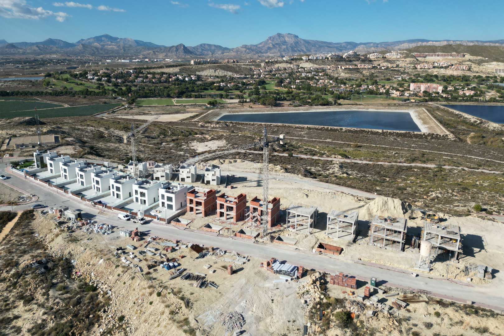 Vista aérea de la promoción en construcción que muestra villas en diversas fases de obra, ubicadas en una zona elevada con vistas panorámicas a la montaña.