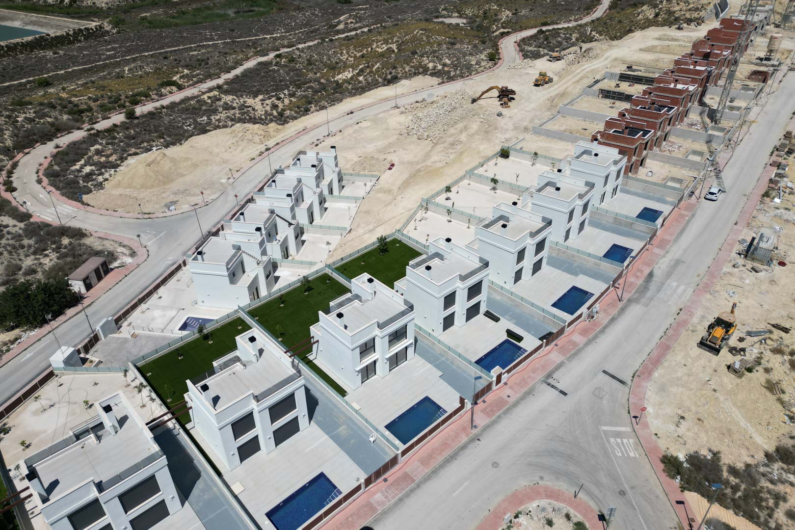 Vista aérea de la urbanización con villas blancas de diseño cúbico, piscinas individuales y parcelas privadas en una zona elevada rodeada de paisaje natural.