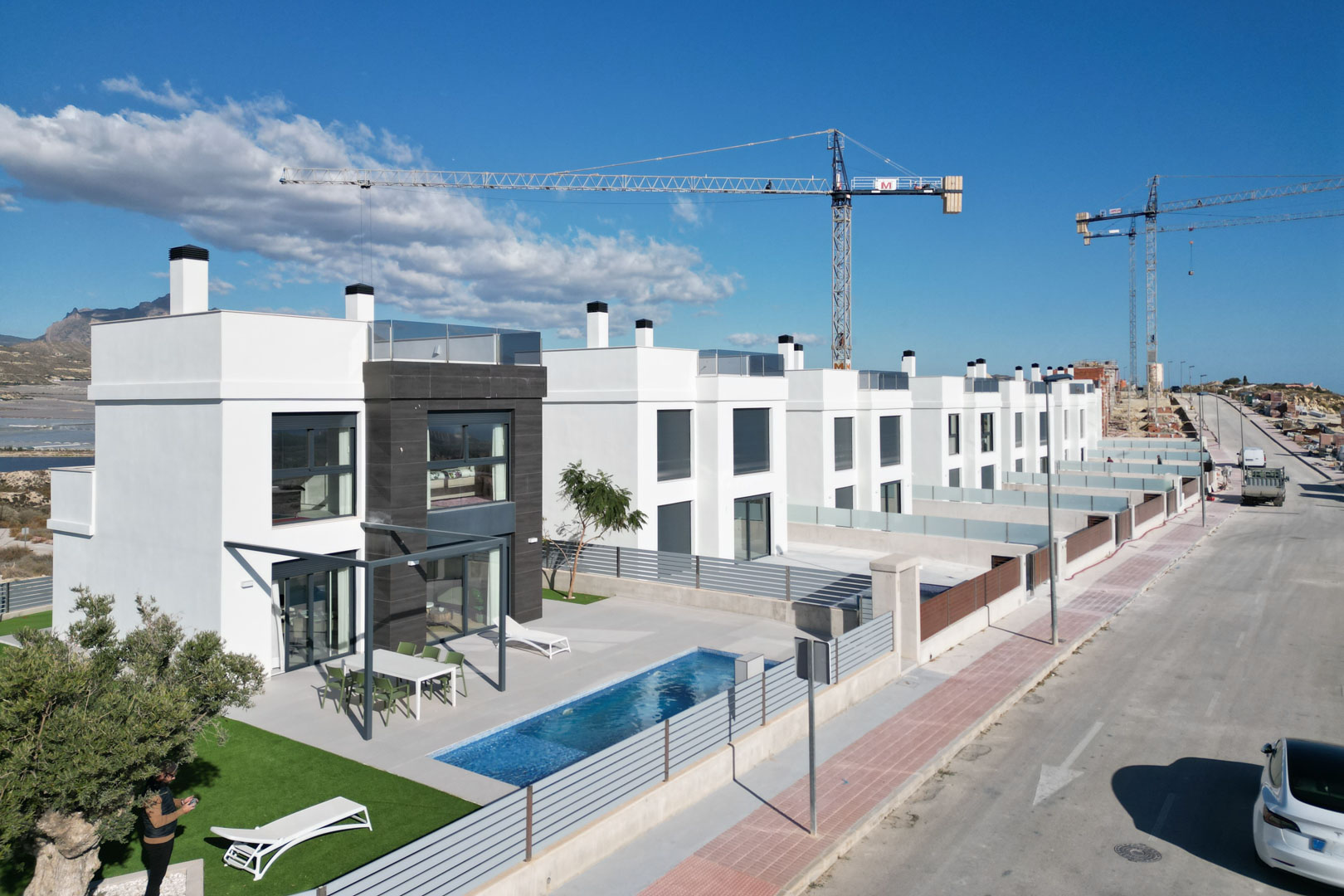 Vista aérea de villas contemporáneas con fachada blanca y piedra oscura, piscina privada, terraza amueblada y solárium superior en un entorno elevado.