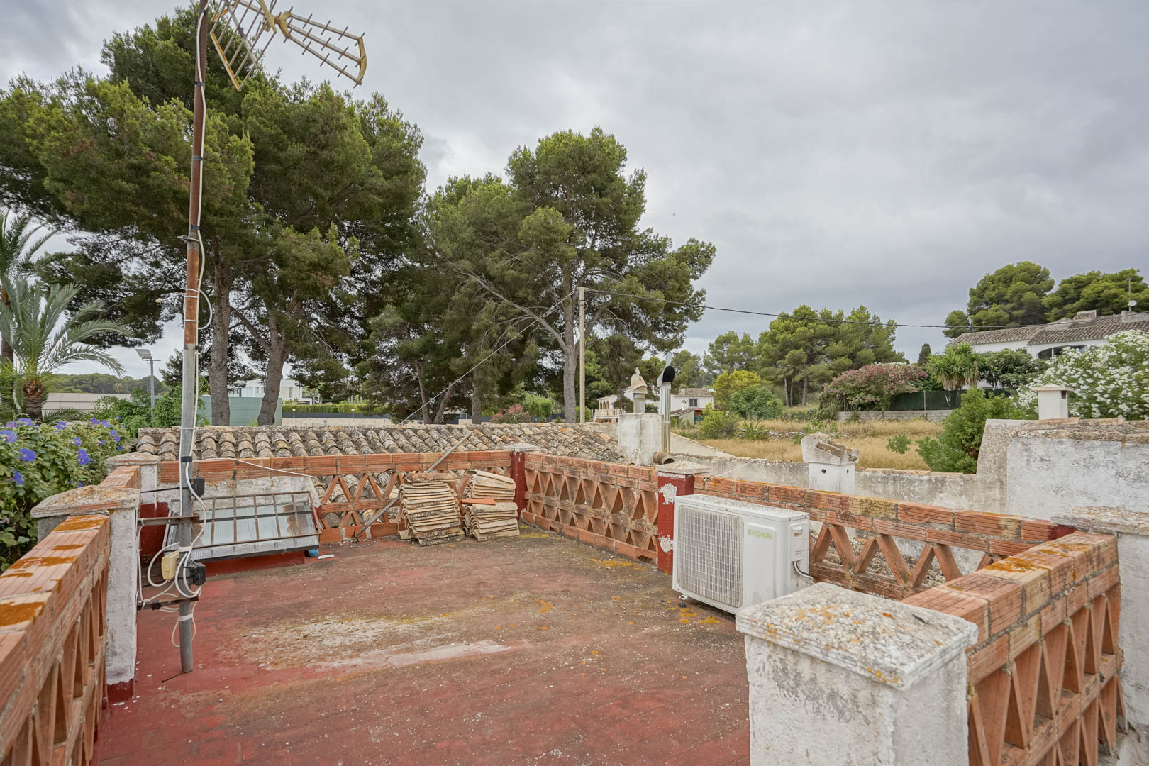 Azotea transitable con suelo de baldosa roja y balaustrada de ladrillo visto. Ofrece vistas despejadas a los pinos circundantes y al entorno residencial de Jávea.