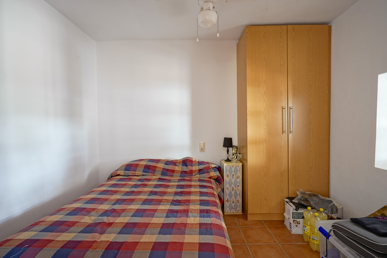 Dormitorio funcional con suelos de baldosas de terracota, armario de madera de gran altura y paredes blancas que maximizan la luz natural.
