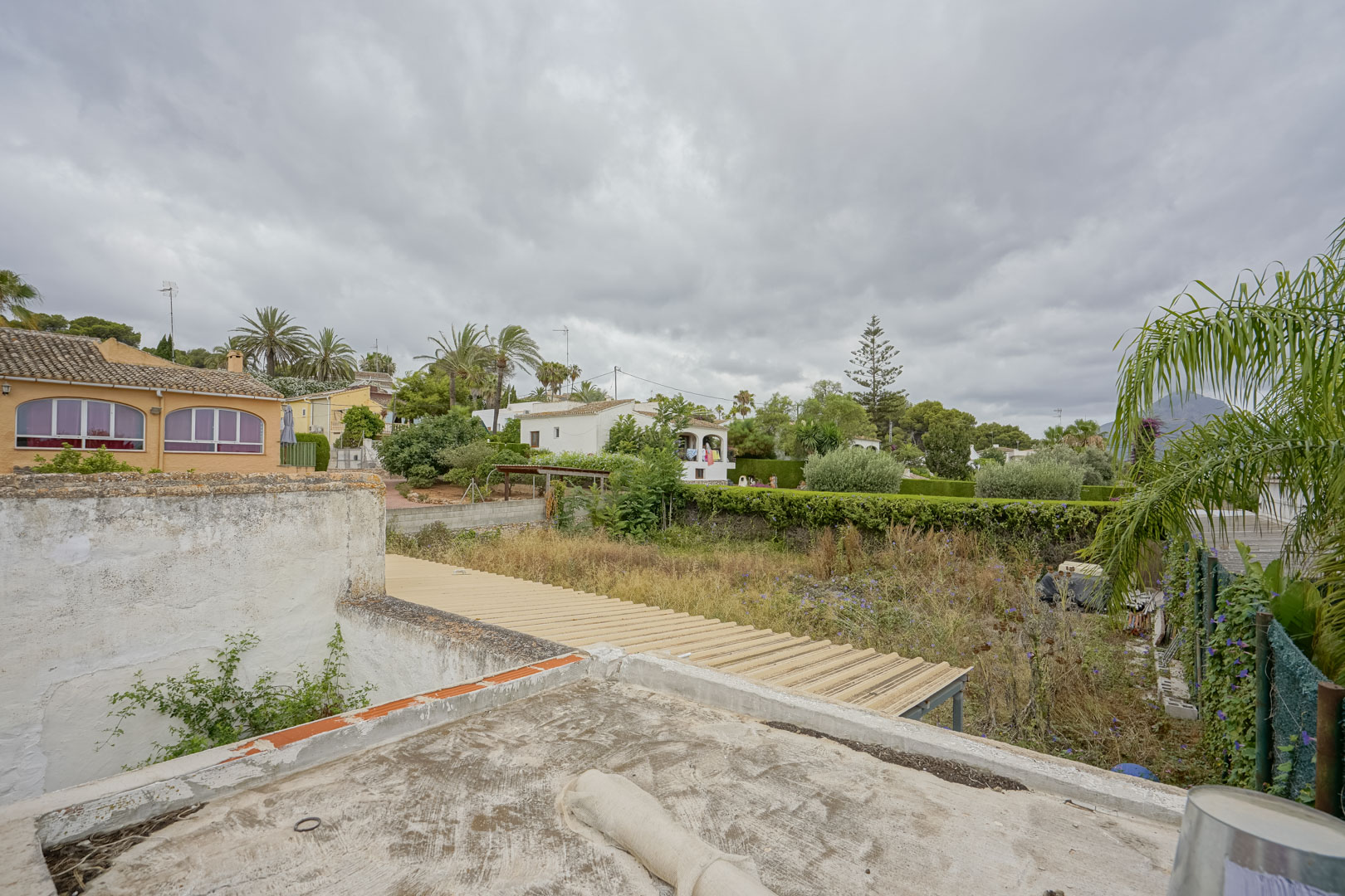 Vista elevada de la parcela de 2.600 m² que muestra su extensión y vegetación natural, con villas colindantes y el perfil del Montgó al fondo.