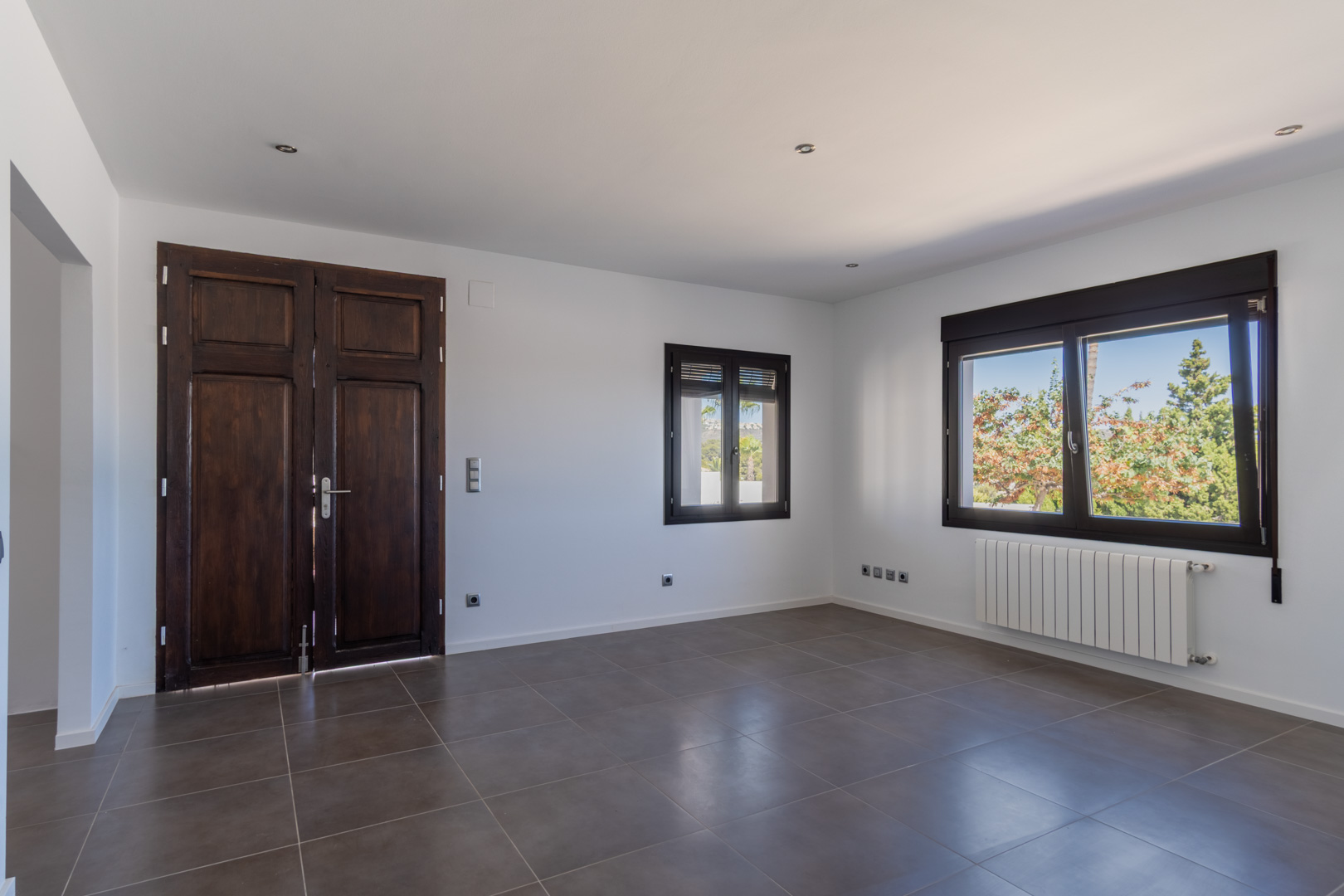 Estancia con puerta antigua de madera restaurada, ventanas de aluminio con acabado efecto madera, calefacción por radiador y suelos cerámicos en tonos grises.