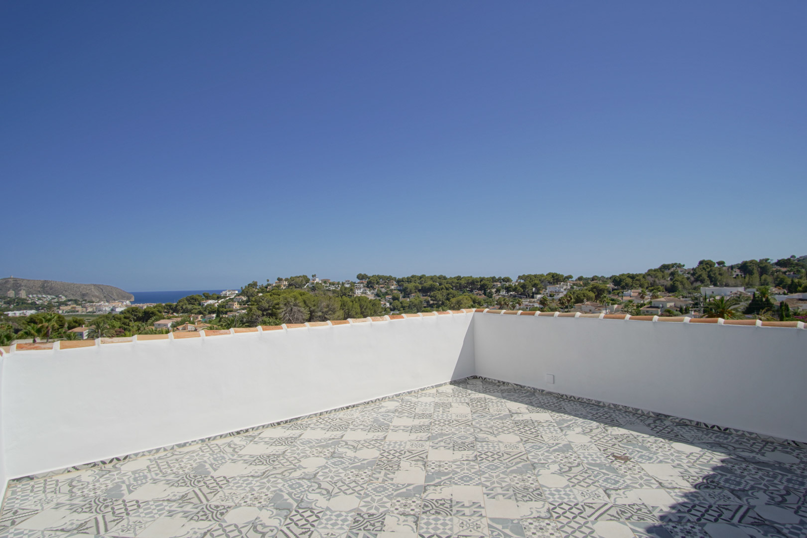 Terraza solárium con suelo de baldosa hidráulica decorativa y vistas panorámicas al mar, la costa de Moraira y el entorno natural circundante.