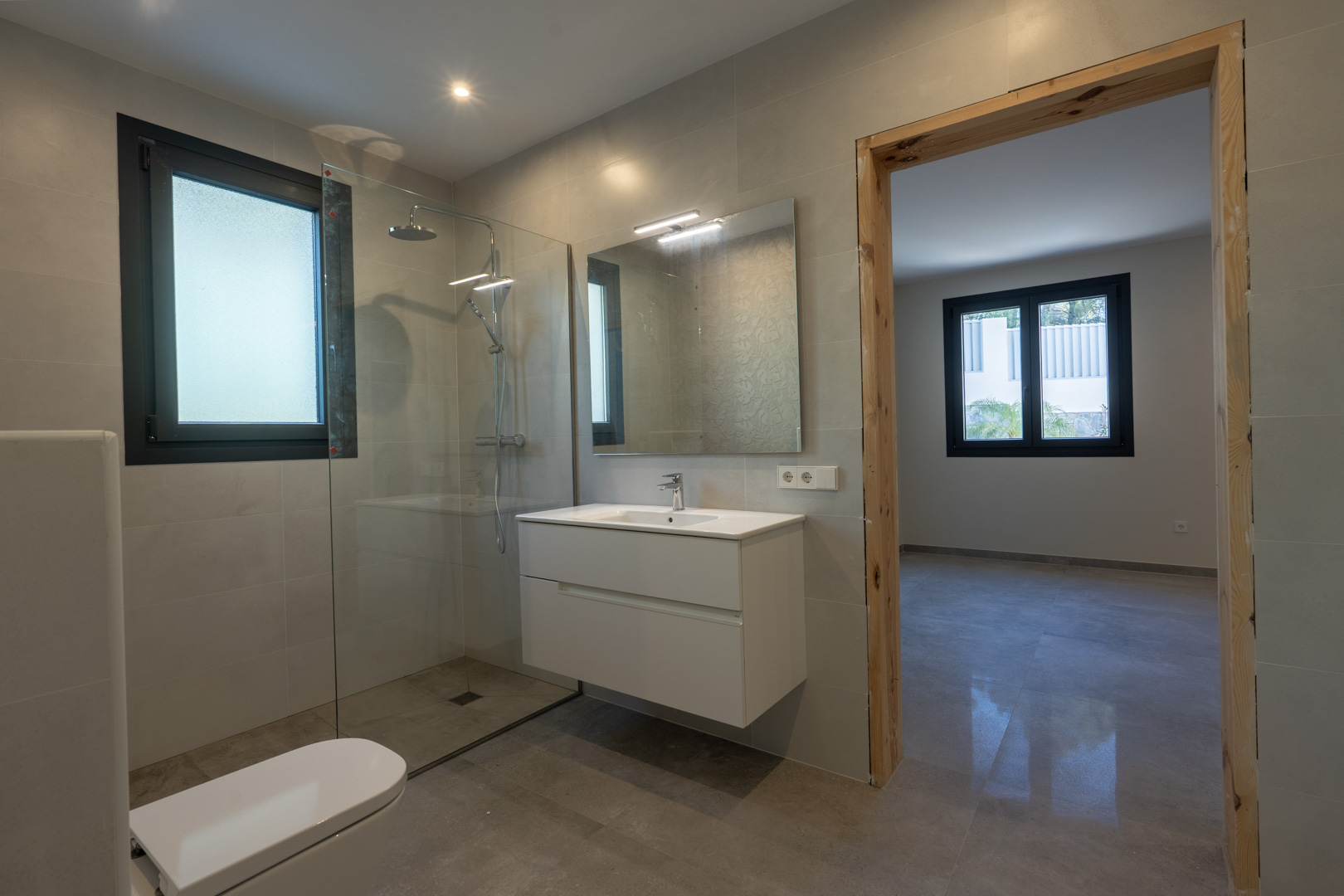Detalle de baño moderno: ducha con mampara, mueble lavabo suspendido y ventana con luz difusa.