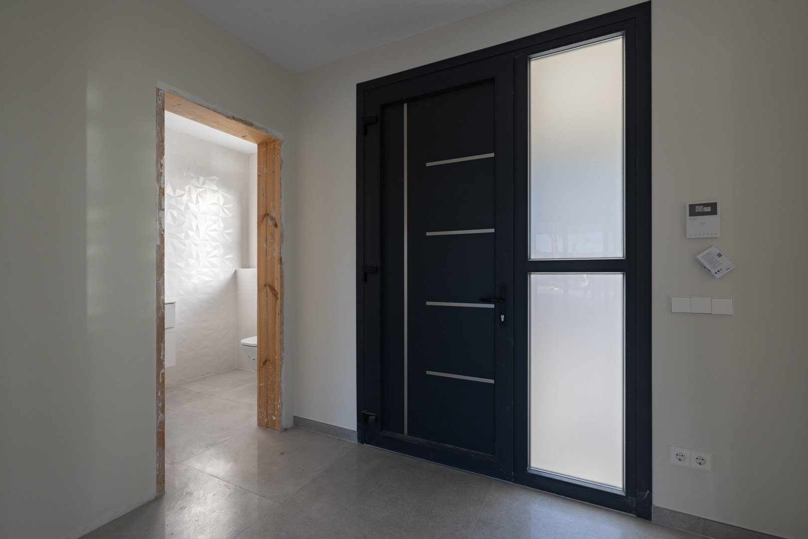 Entrada moderna con puerta de diseño y acceso a aseo con pared de azulejos texturizados.