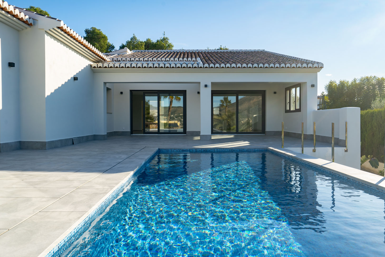 Vista de la piscina privada con mosaicos azules y la terraza de baldosas grises de la villa.