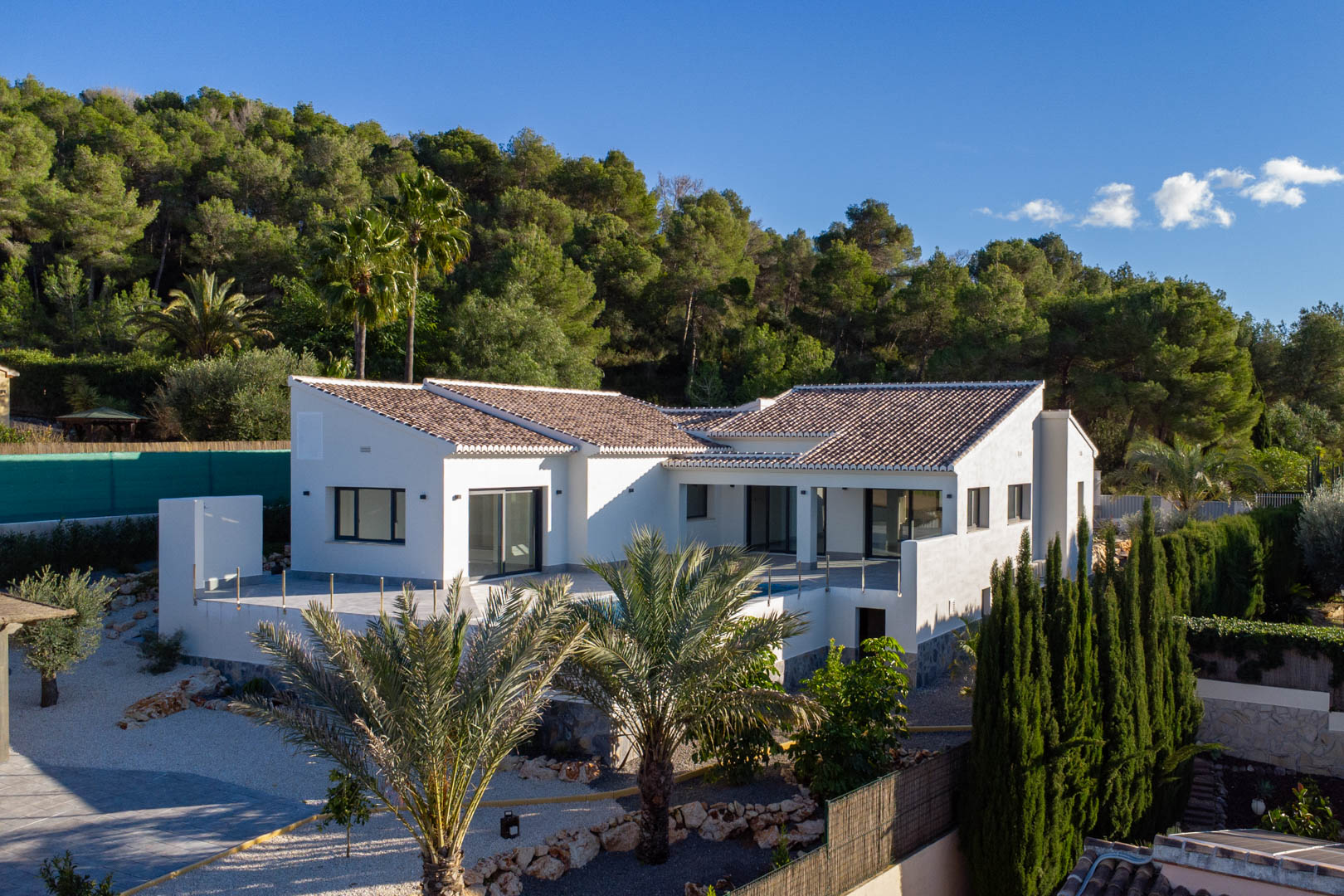 Vista exterior de la villa de obra nueva en Jávea, destacando su diseño moderno y piscina privada rodeada de vegetación.