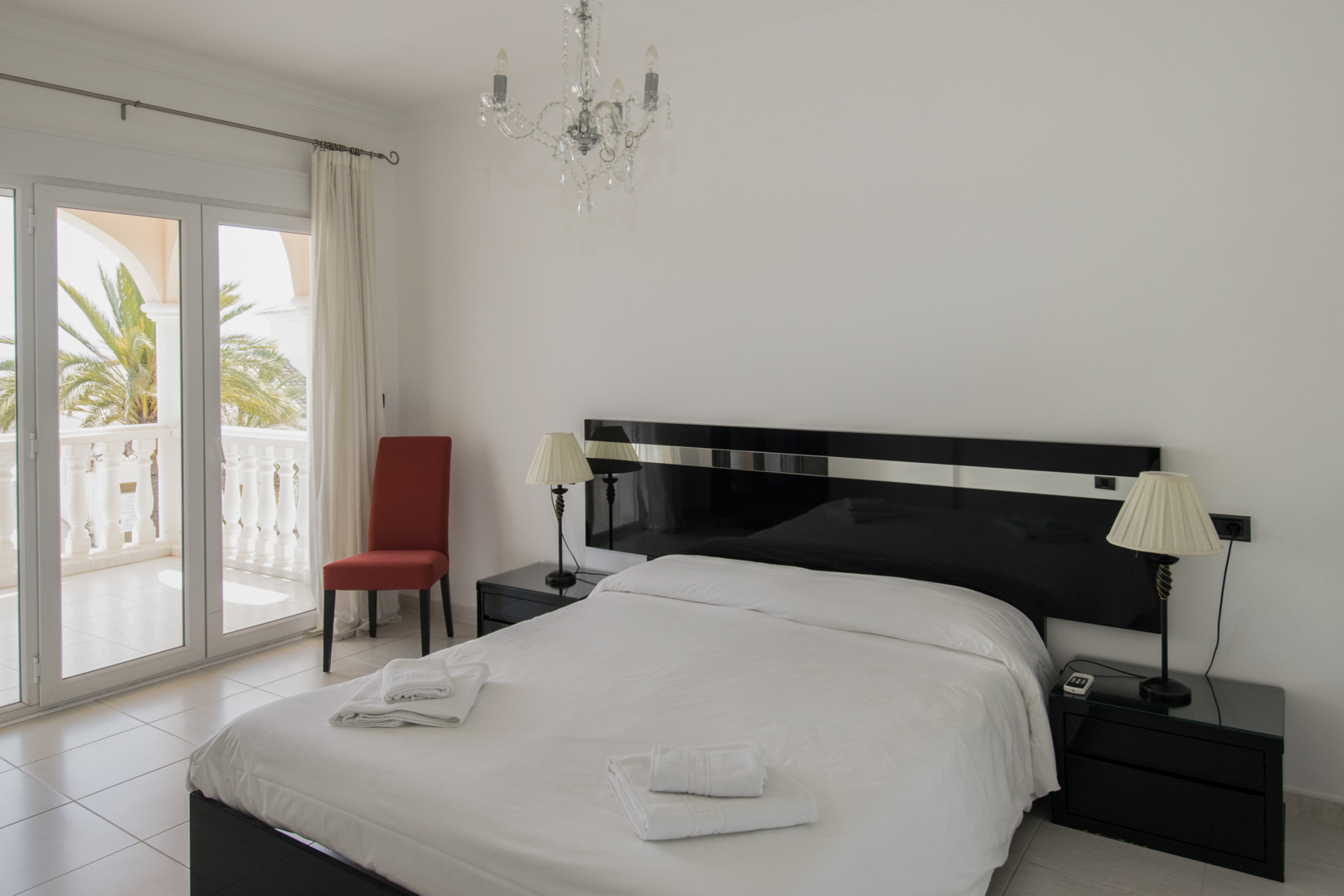 Dormitorio con cama doble, cabecero negro lacado y acceso directo a una terraza privada con vistas a la vegetación mediterránea y balaustrada.