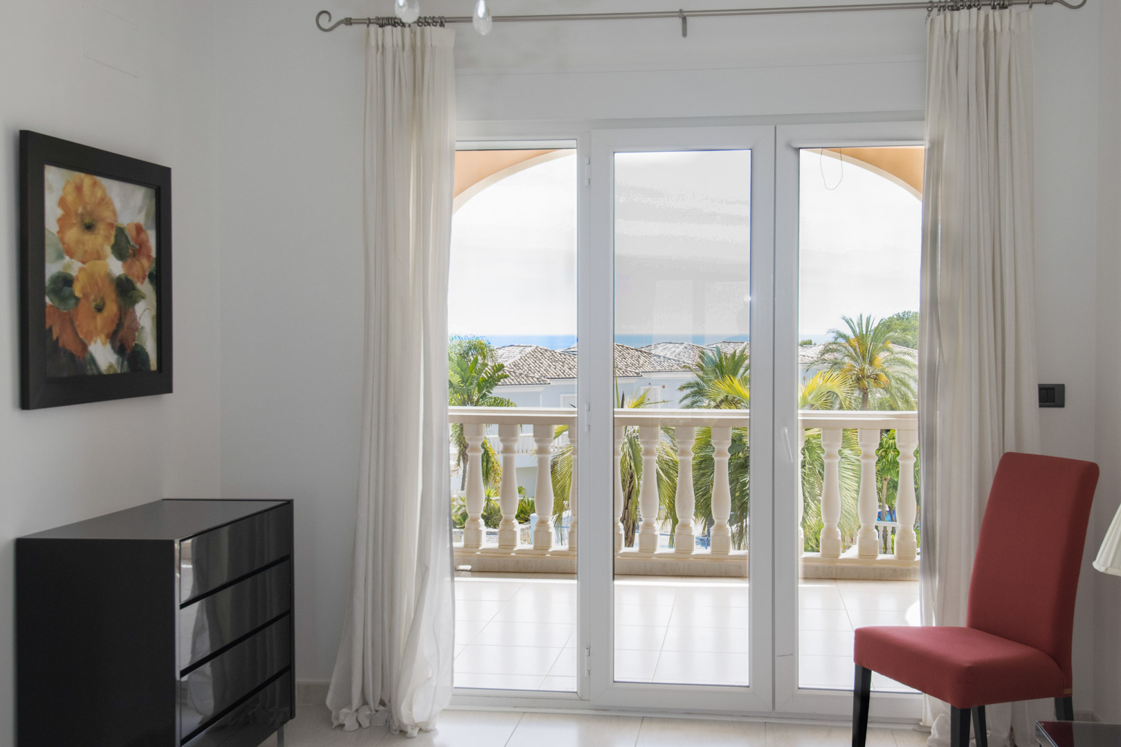 Vista desde el interior hacia la terraza privada con balaustrada de piedra, palmeras y vistas parciales al mar a través de grandes puertas acristaladas.
