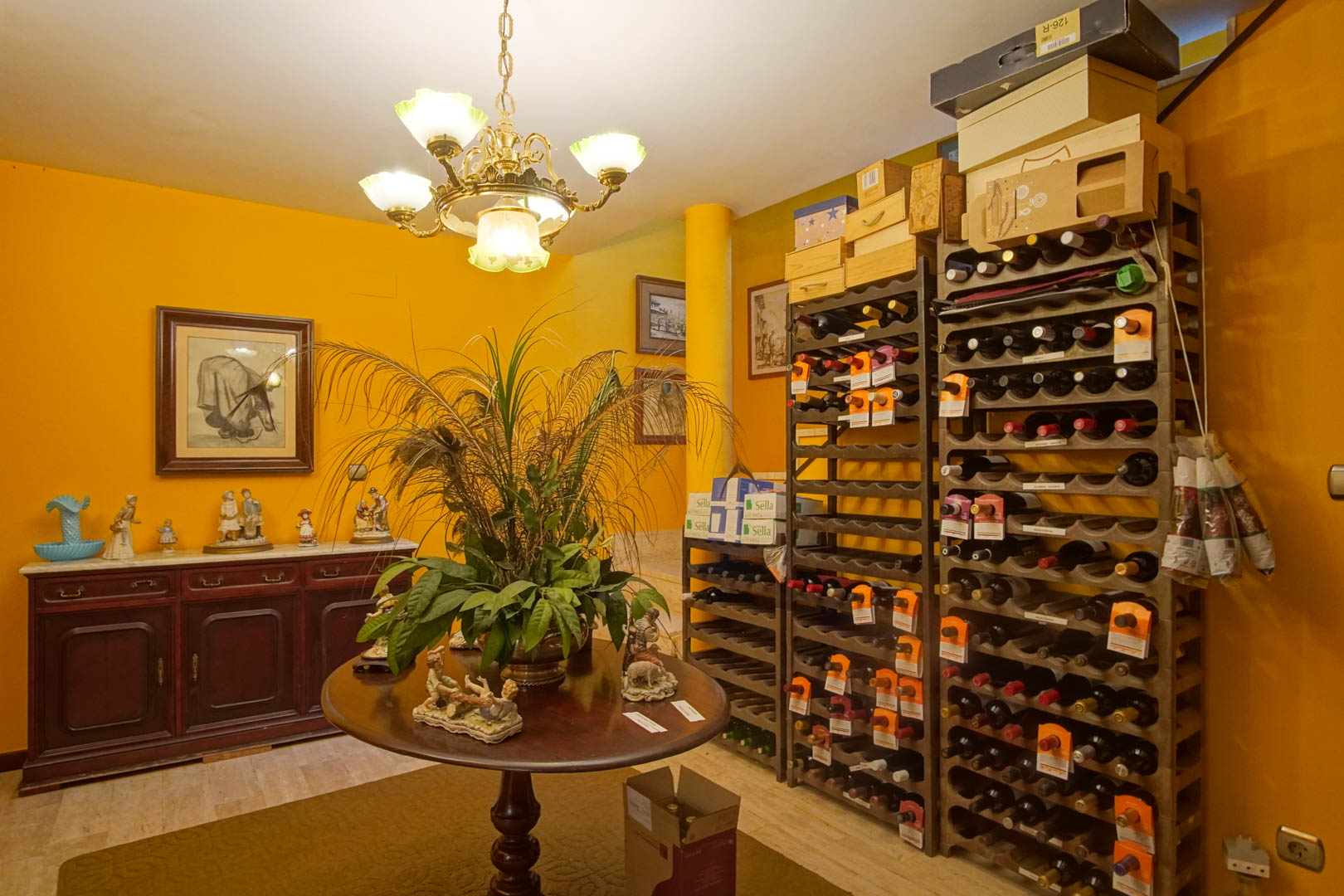 Bodega interior equipada con estanterías verticales para botellas, mesa central de madera y aparador clásico sobre suelos de mármol y paredes ocre.