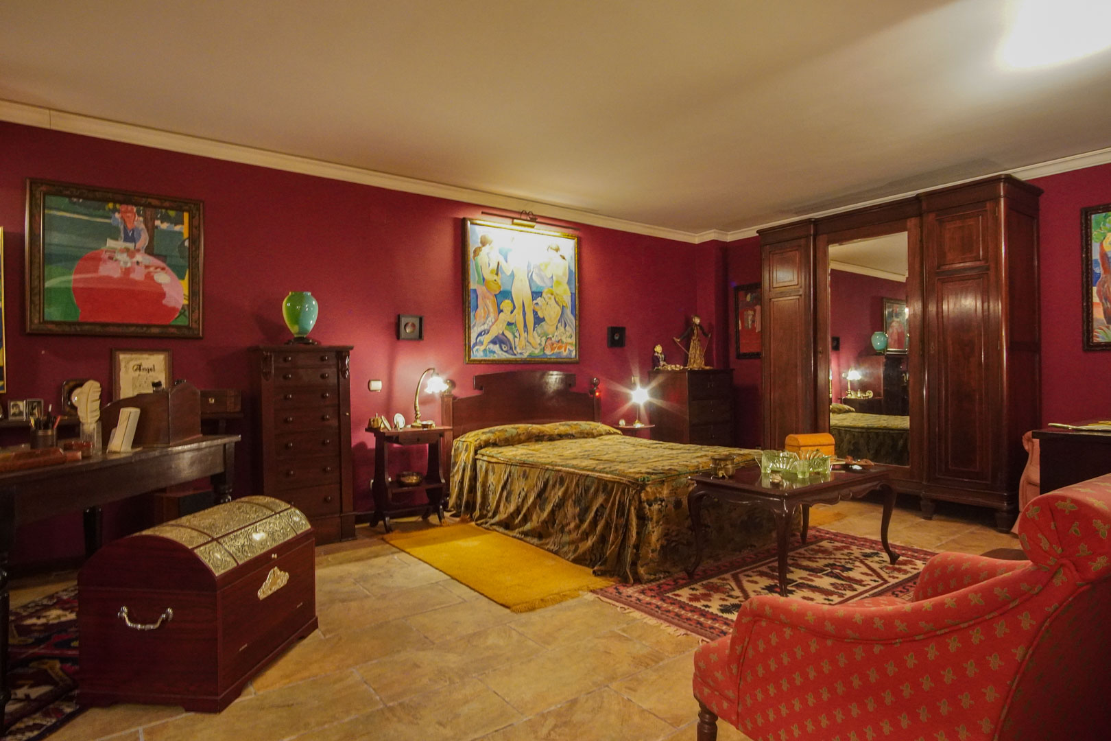 Dormitorio de estilo clásico con paredes burdeos, mobiliario de madera oscura, suelos de piedra natural y un amplio armario con espejo central.
