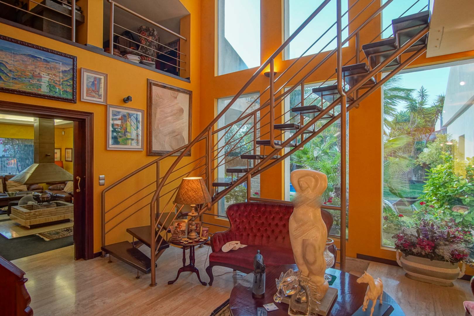 Salón de doble altura con escalera de diseño de peldaños volados, grandes ventanales con vistas al jardín mediterráneo y suelos de mármol.