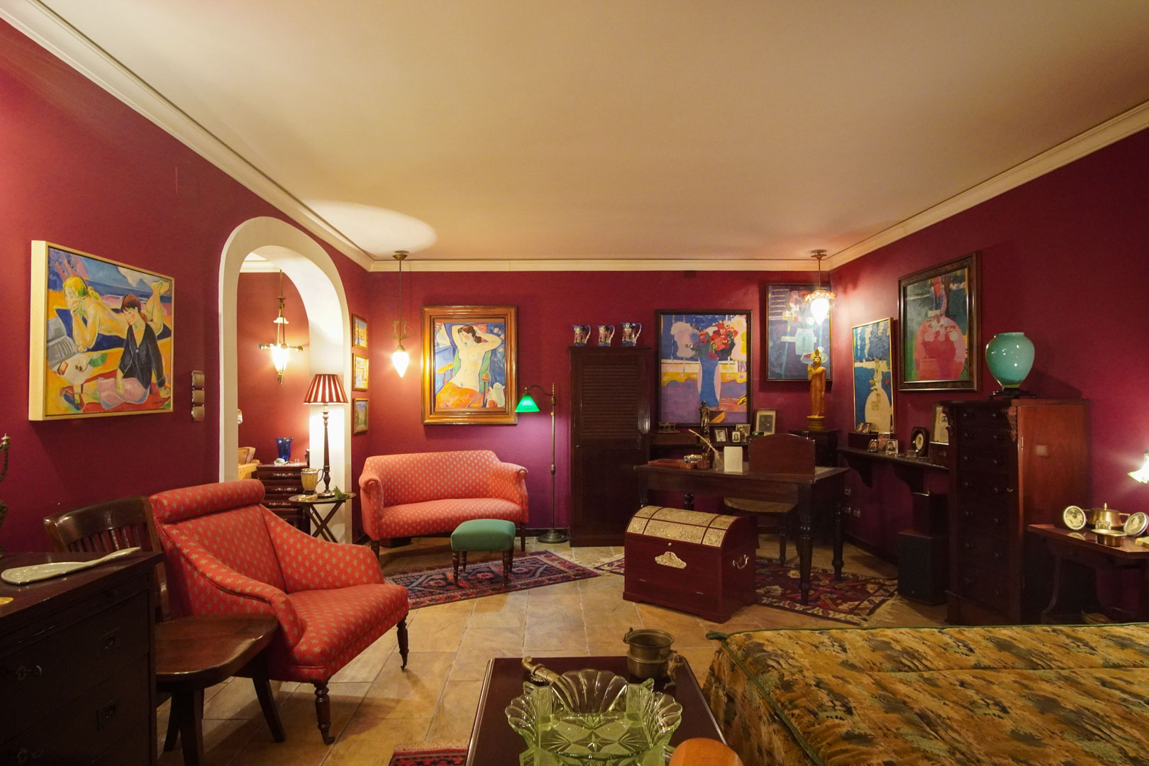 Salón de estilo clásico con paredes granate, suelos de mármol y zona de despacho. Destaca la colección de arte, el mobiliario de época y el acceso mediante arco de medio punto.