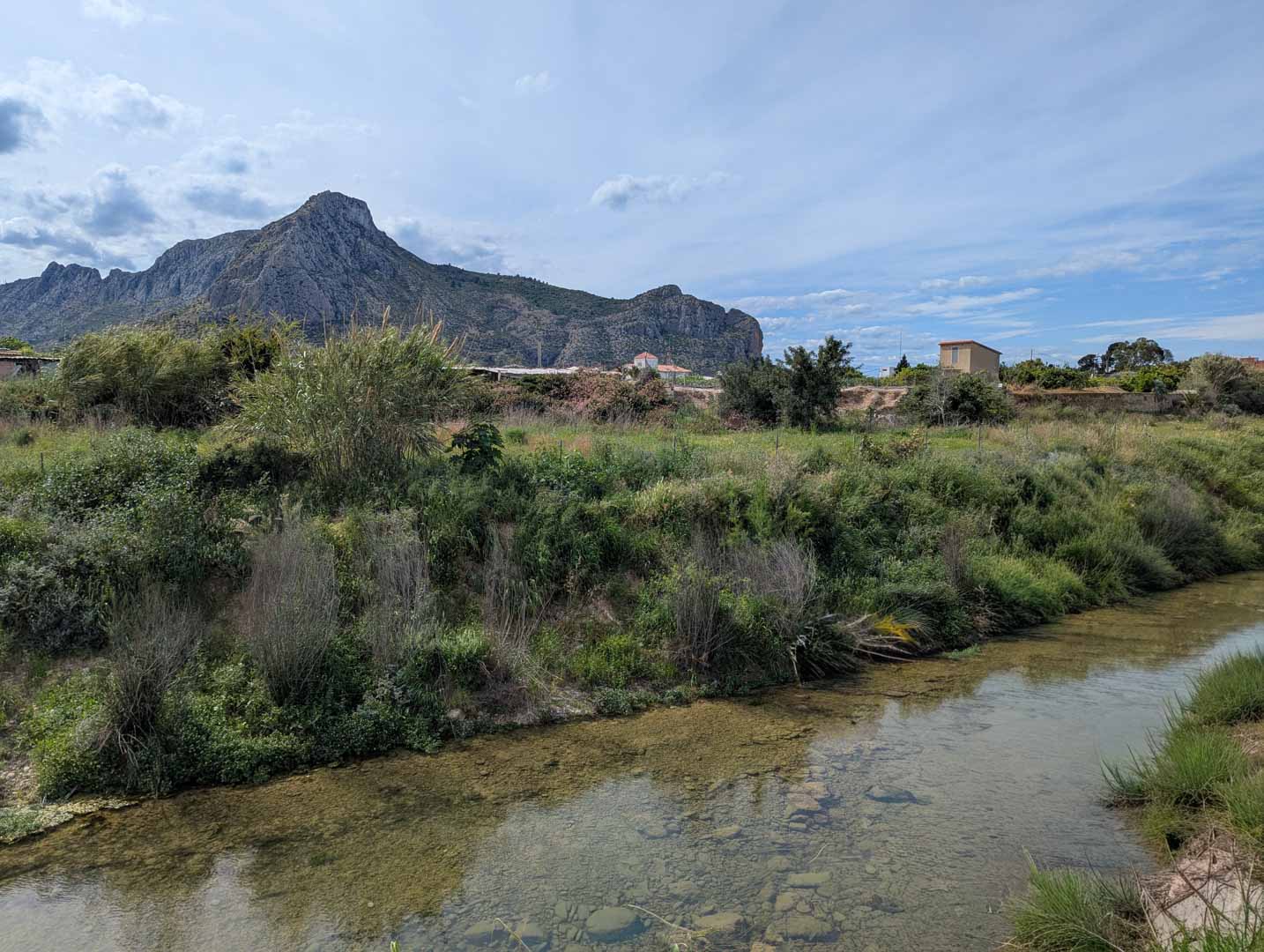 Vista del entorno natural colindante con un arroyo de aguas claras y vegetación autóctona, bajo la silueta de la Sierra de Segaria.
