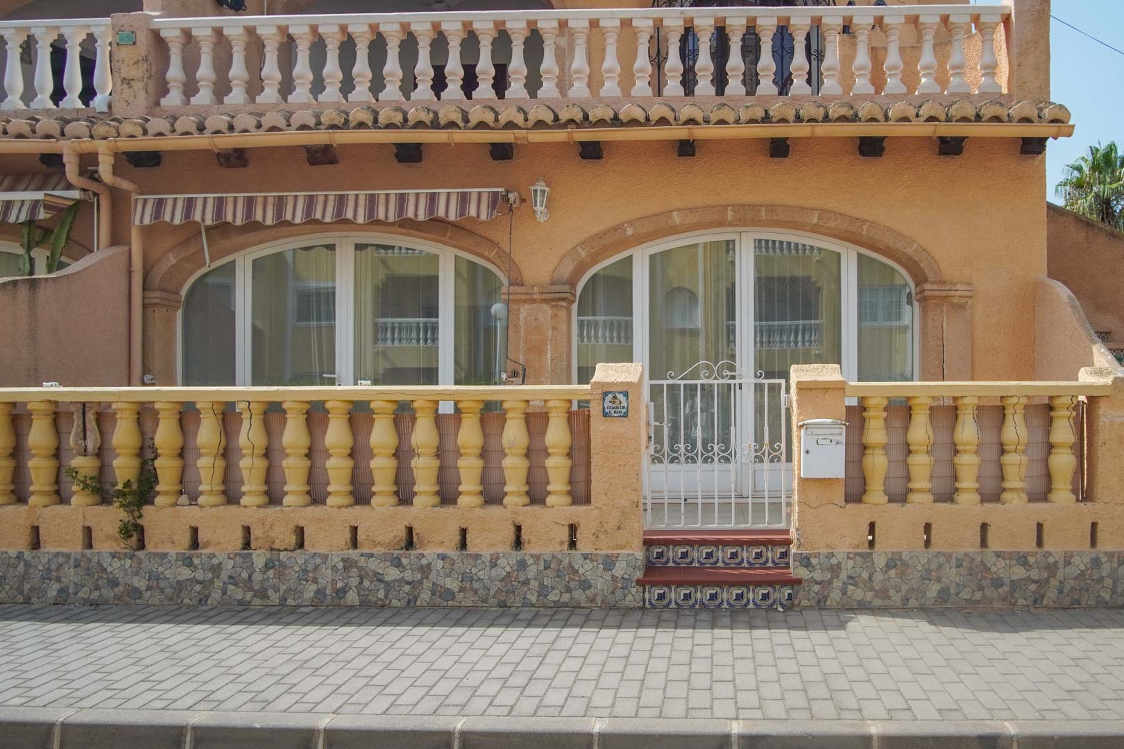 Fachada exterior de planta baja con balaustrada clásica, acceso mediante puerta metálica blanca y grandes ventanales en arco que dan paso a la terraza.