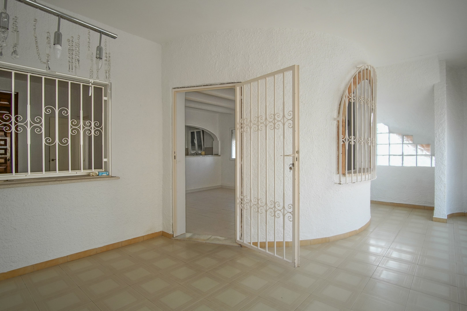 Terraza cubierta con suelos cerámicos, paredes blancas de acabado rugoso y carpintería metálica de seguridad en puertas y ventanas de arco.