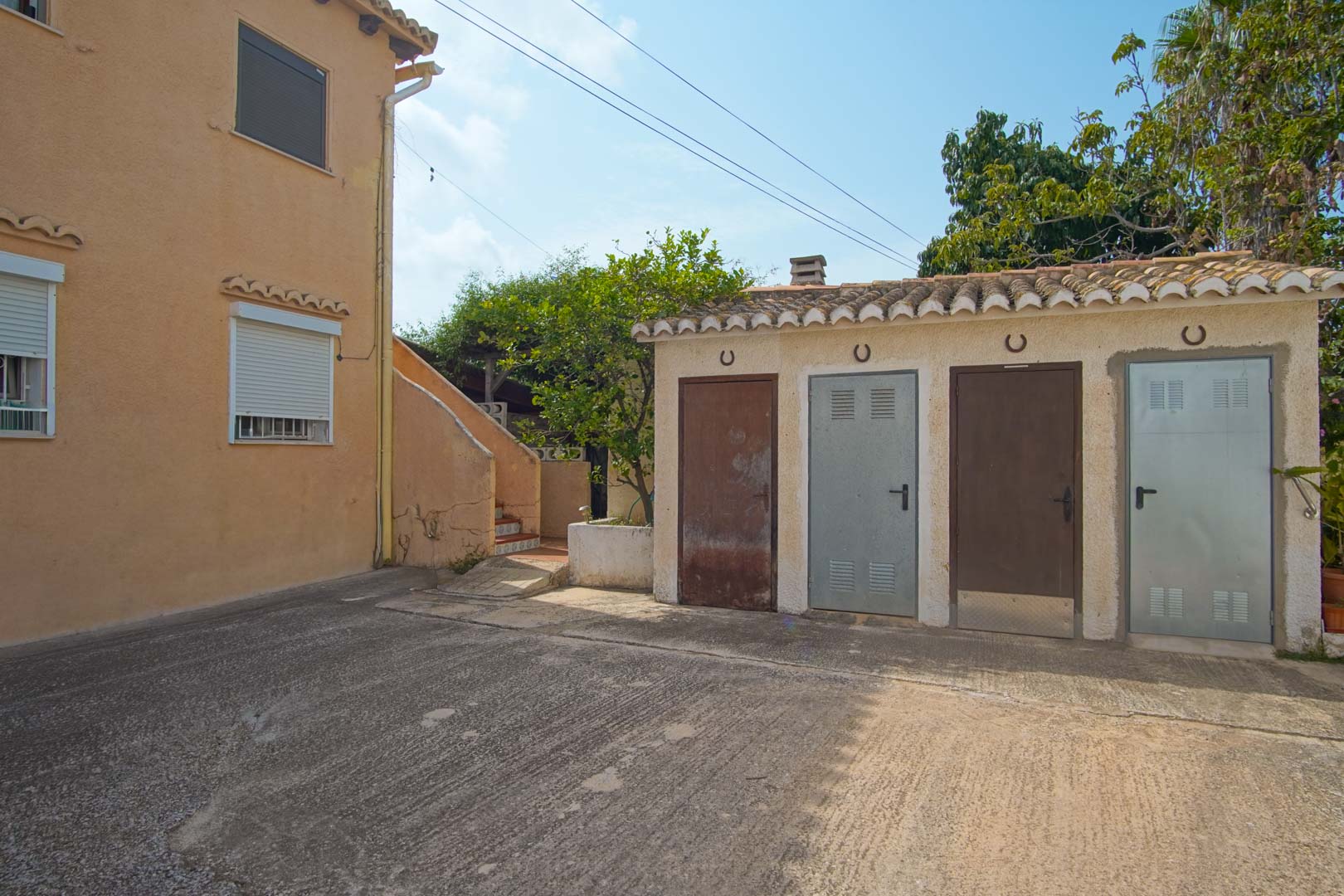 Zona exterior pavimentada con un anexo funcional que alberga cuatro trasteros independientes, identificados con herraduras decorativas bajo un tejado de teja árabe.
