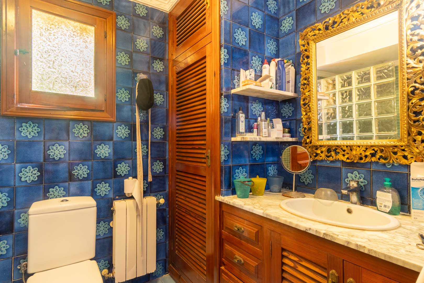 Cuarto de baño con azulejos azules ornamentados, mueble de lavabo en madera con encimera de mármol y un espejo de marco dorado labrado de estilo clásico.