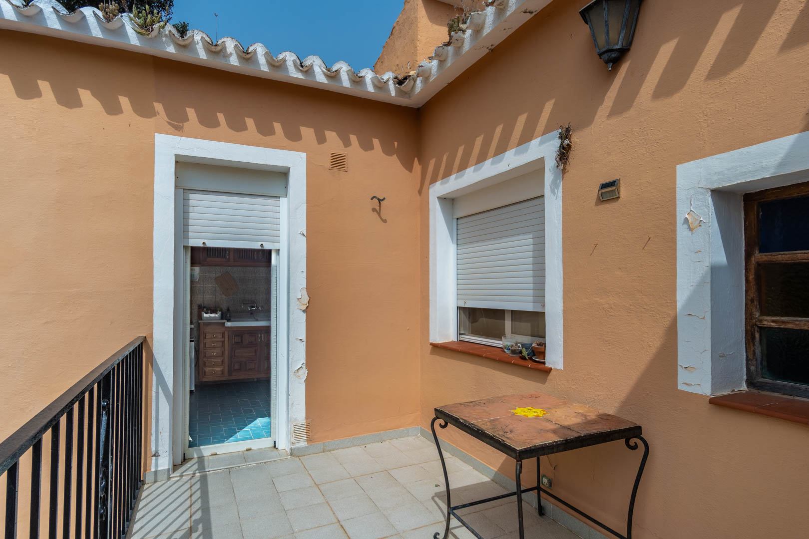 Terraza superior con suelo de gres y barandilla de forja, que comunica directamente con la cocina independiente a través de una puerta con persiana.