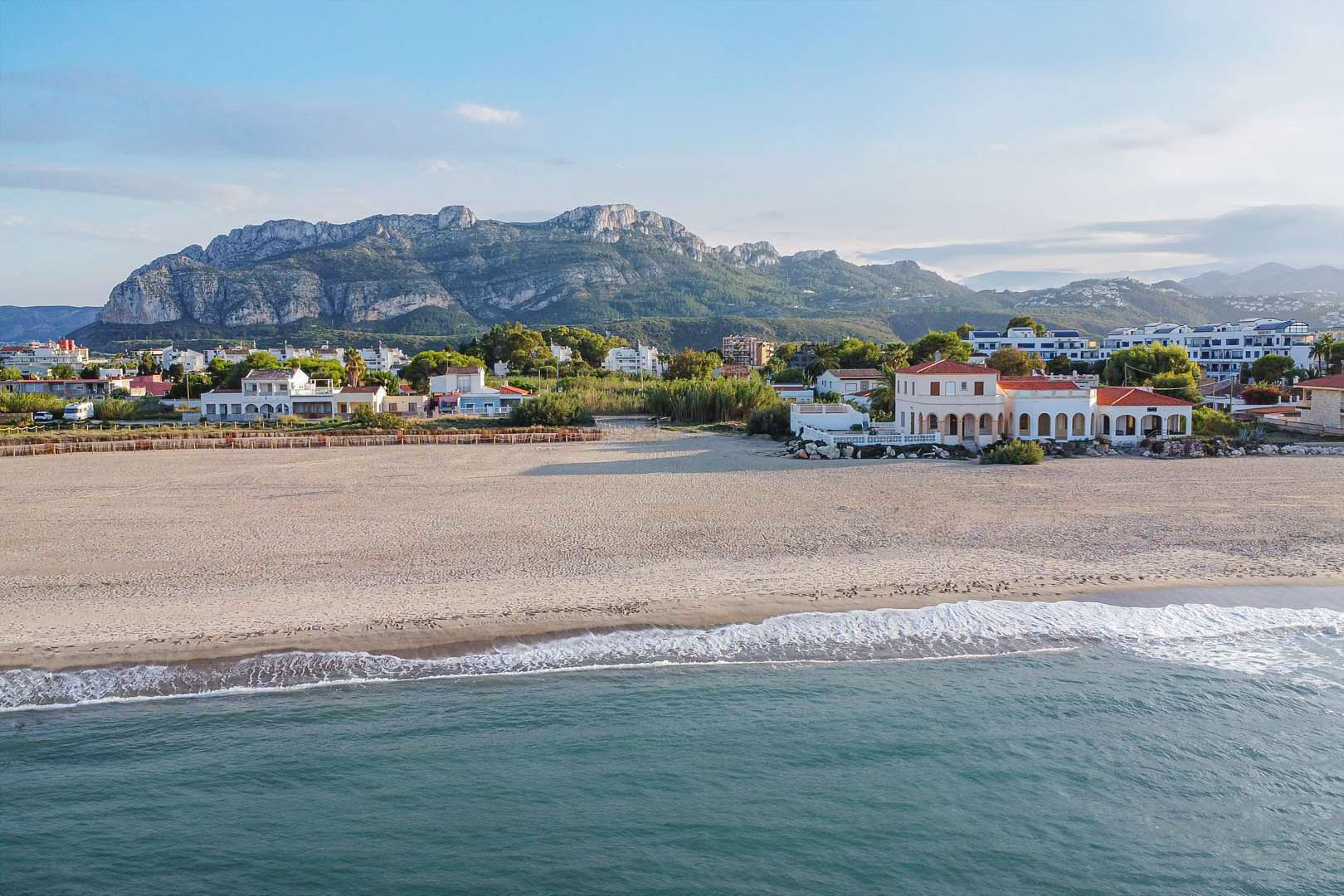 Vista aérea de la playa de Las Marinas con el macizo del Montgó al fondo, destacando la proximidad de las viviendas al mar y la amplitud de la costa arenosa.