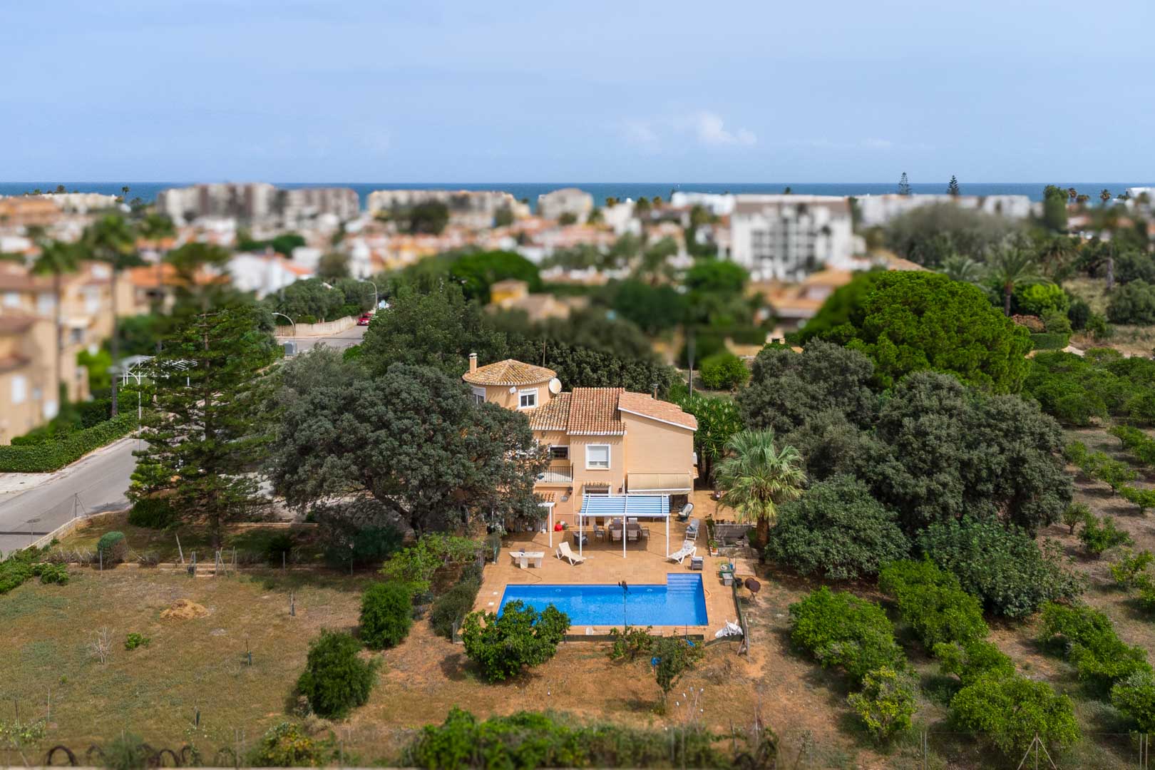 Vista aérea del chalet mediterráneo en Las Marinas, destacando su amplia parcela llana con piscina, terrazas y frondosa vegetación con el mar al fondo.
