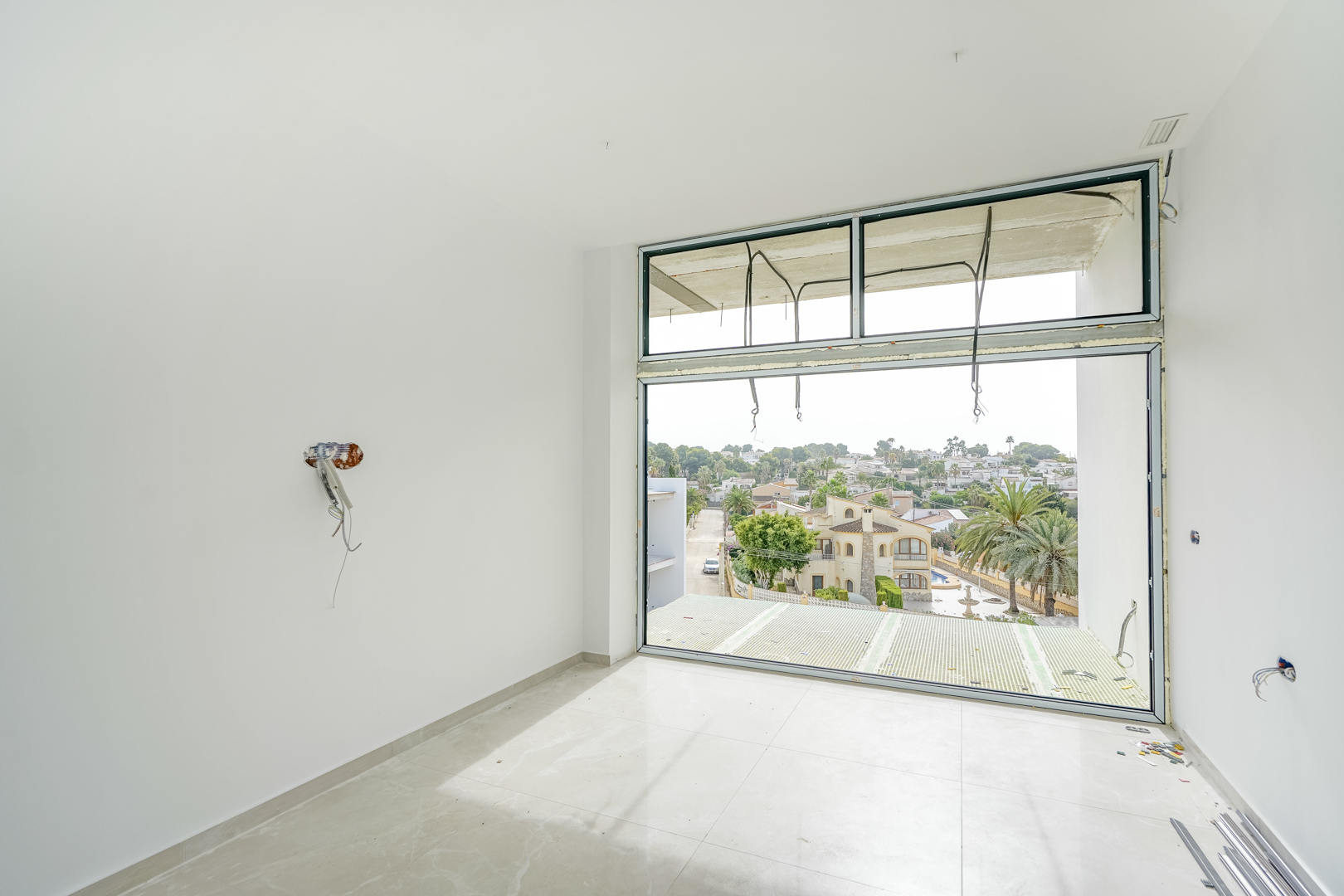 Habitación en construcción con amplios ventanales de suelo a techo, suelos de gres porcelánico claro y vistas despejadas a la urbanización Partida La Merced.