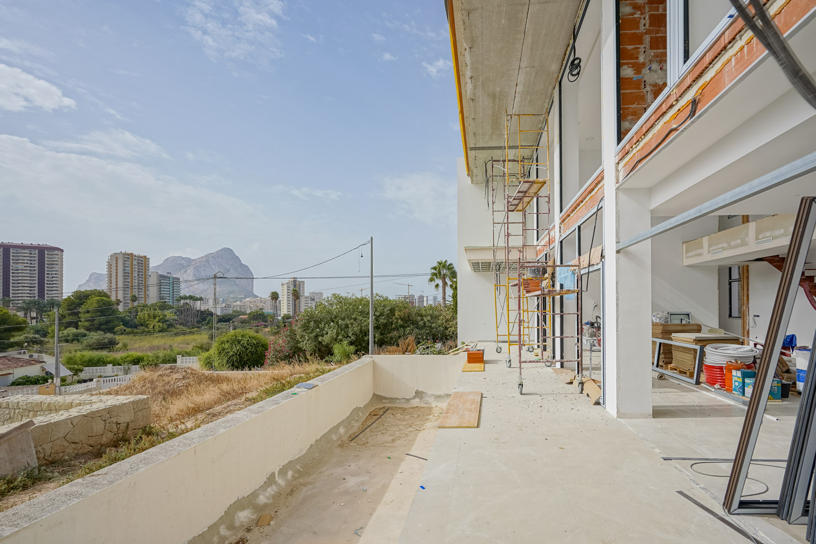Vista exterior de la villa en construcción con andamios, mostrando los amplios ventanales y la terraza con vistas directas al Peñón de Ifach en Calpe.