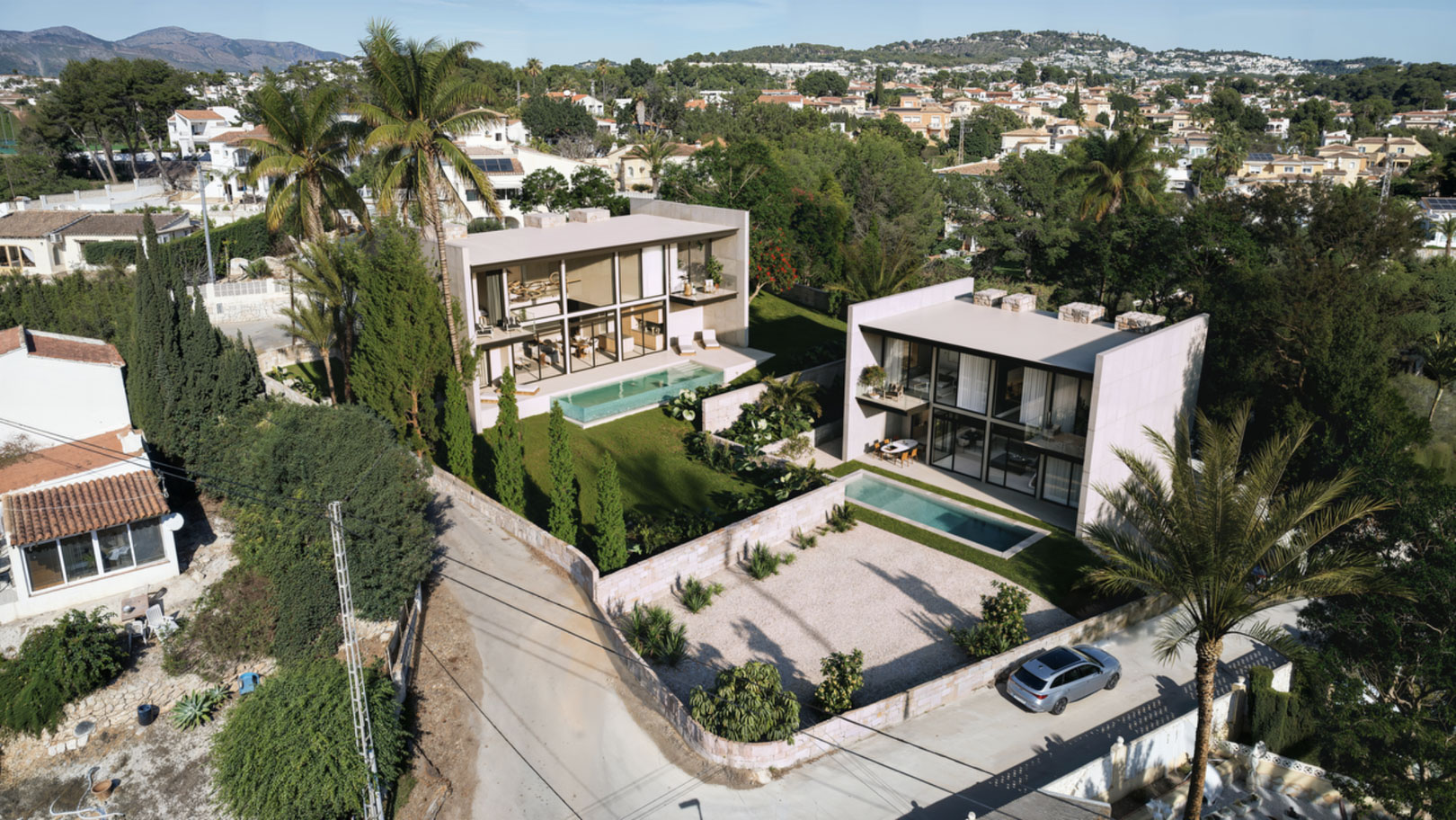 Vista aérea de dos villas modernas con fachadas de cristal, piscinas privadas y jardines mediterráneos integrados en la tranquila urbanización de Calpe.