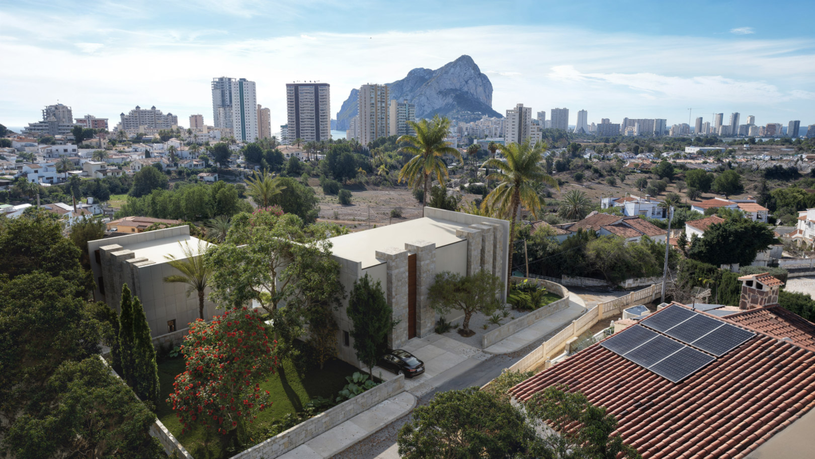 Vista aérea de la villa moderna con fachada de piedra natural, rodeada de jardines y con el Peñón de Ifach destacando en el horizonte de Calpe.