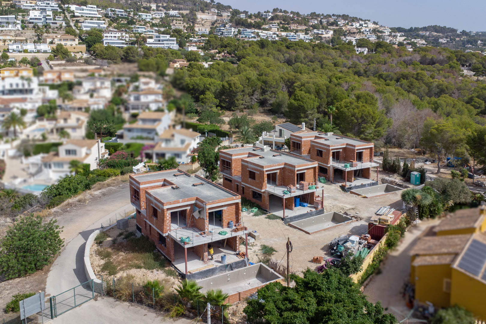 Vista aérea de las tres villas de lujo en fase de construcción estructural, mostrando la tabiquería de ladrillo y los huecos para las piscinas privadas en parcelas individuales.