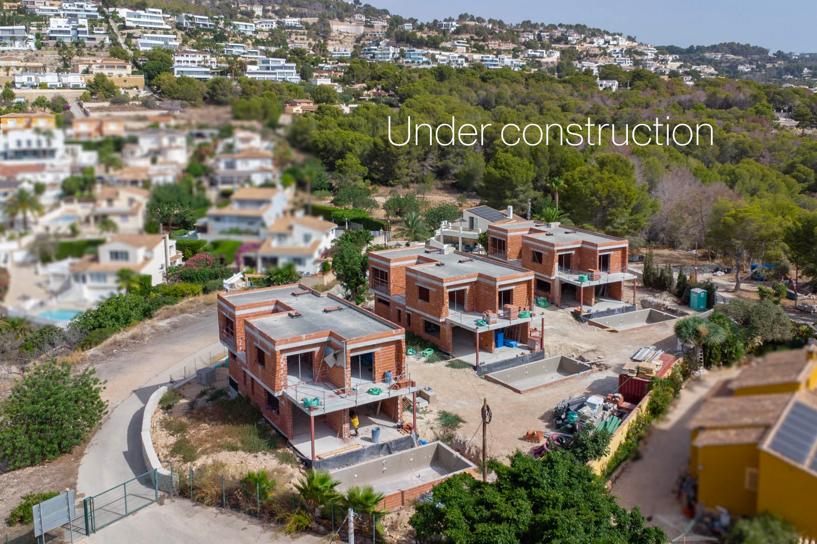 Vista aérea de las tres villas en construcción en Calpe, mostrando las estructuras de ladrillo, forjados de hormigón y excavaciones para las piscinas privadas.