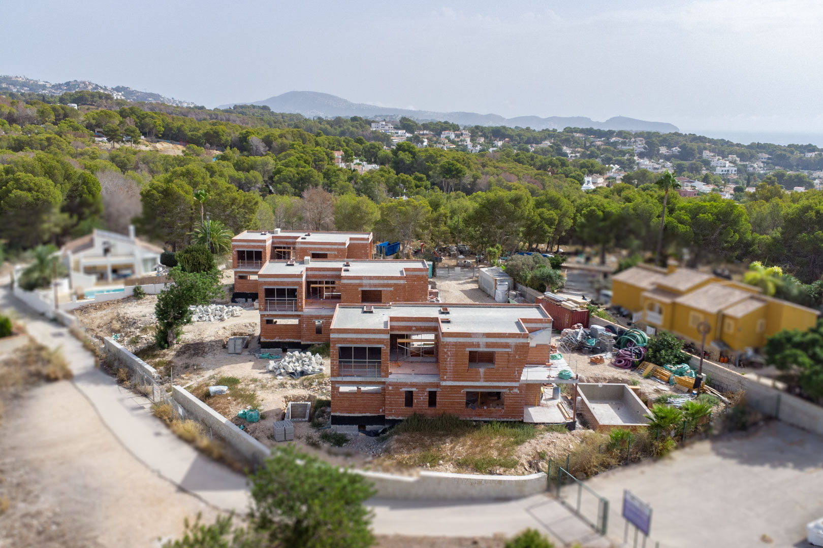 Vista aérea del estado actual de construcción de las tres villas, mostrando la estructura de ladrillo, las parcelas llanas y el entorno natural cerca de la costa.
