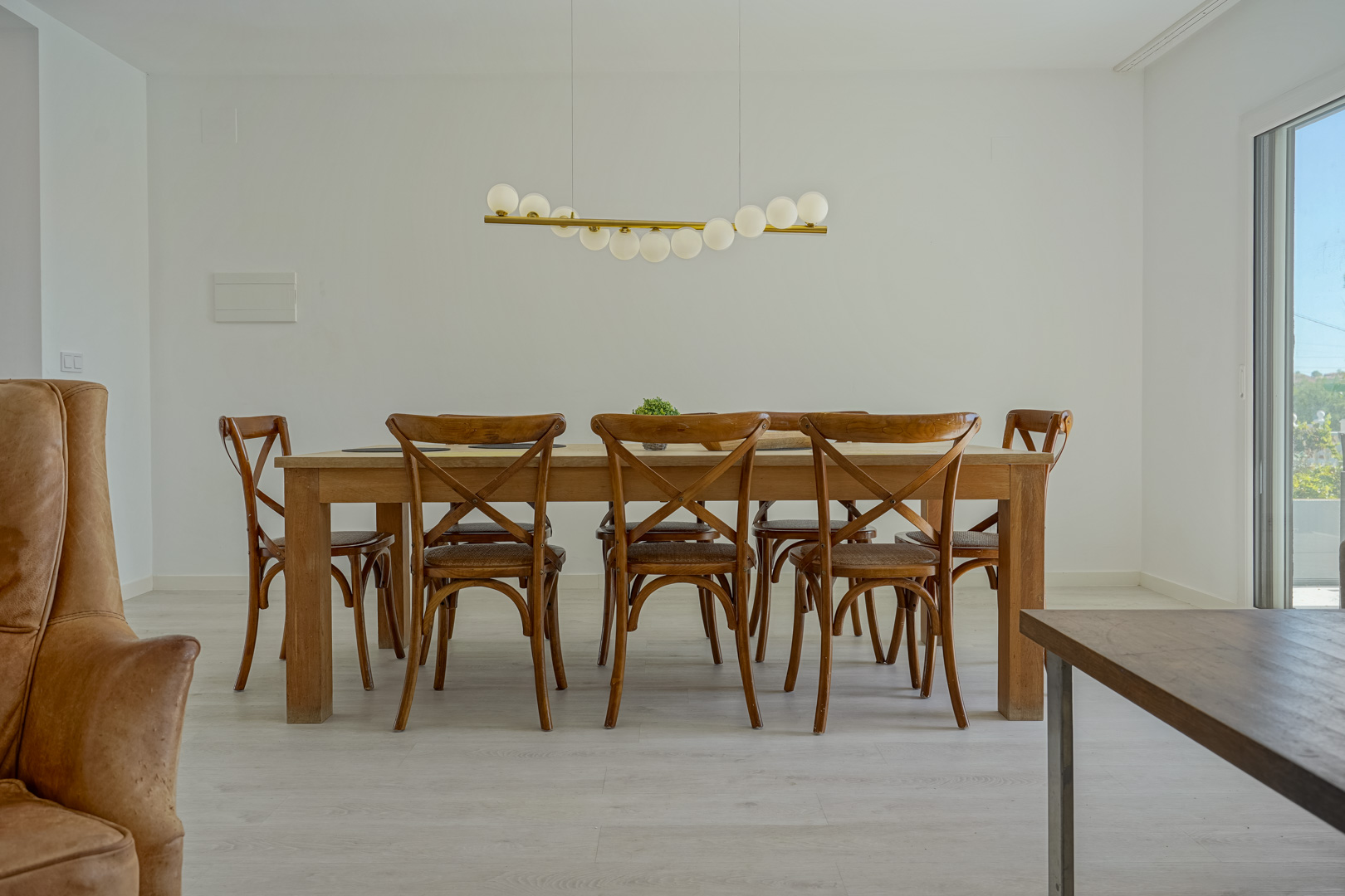 Comedor con mesa de madera maciza y sillas de estilo rústico, iluminado por una lámpara colgante de diseño moderno sobre suelos de madera clara.