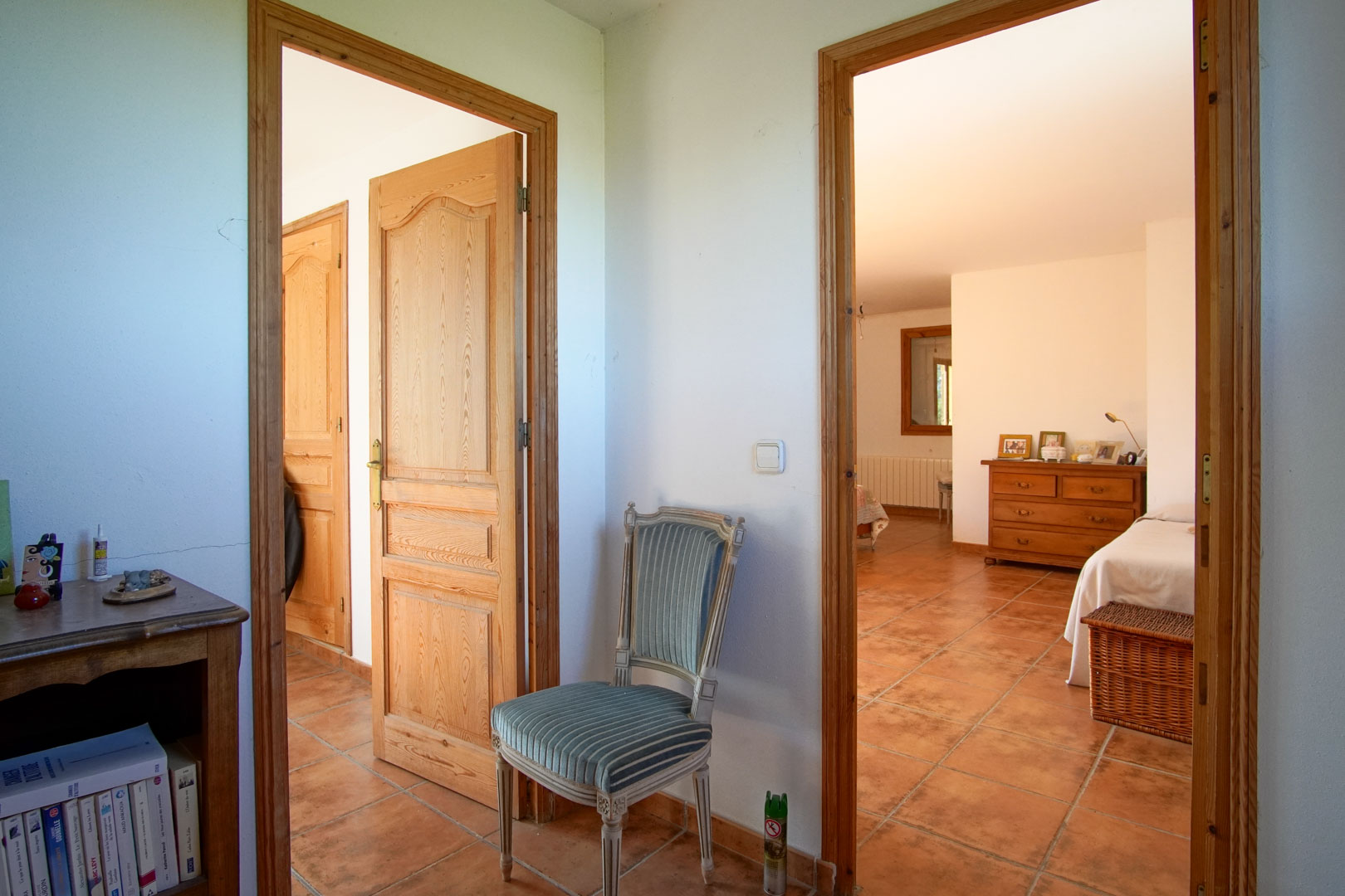 Distribuidor con suelos de gres rústico y carpintería de madera maciza que conecta con dormitorios luminosos y estancias de estilo tradicional mediterráneo.