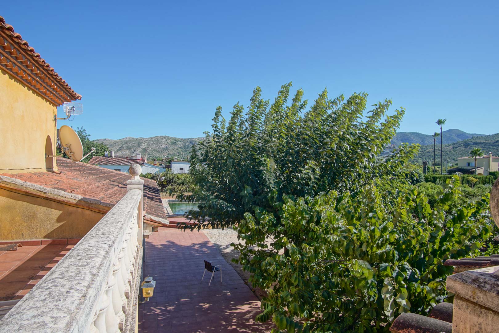 Vista desde la terraza superior con balaustrada de piedra, mostrando el patio de baldosas, la zona de piscina y la vegetación con las montañas de Segaria al fondo.