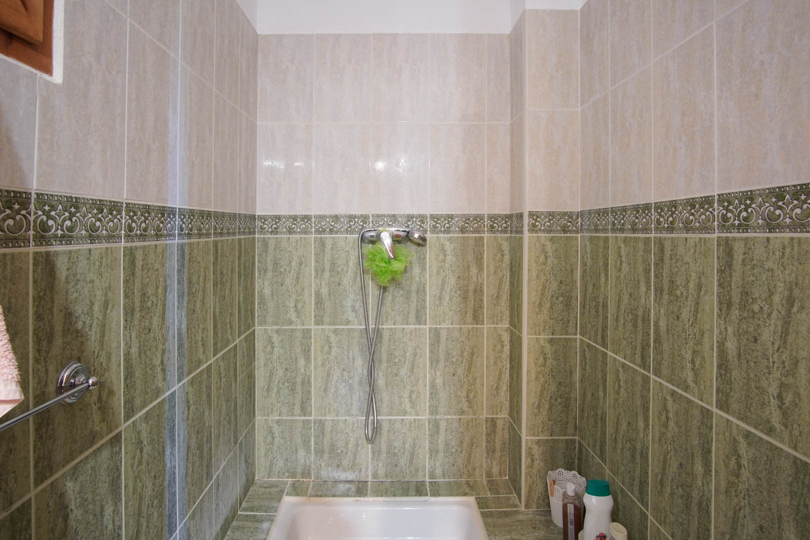 Zona de ducha con alicatado cerámico en dos tonos, verde y crema, divididos por una cenefa decorativa. Incluye plato de ducha blanco y grifería cromada.